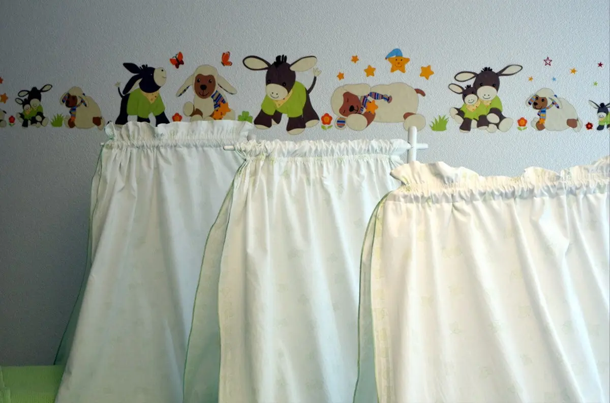 Tende bianche in un ambiente infantile, decorate con adesivi murali raffiguranti animali come asini e cani.