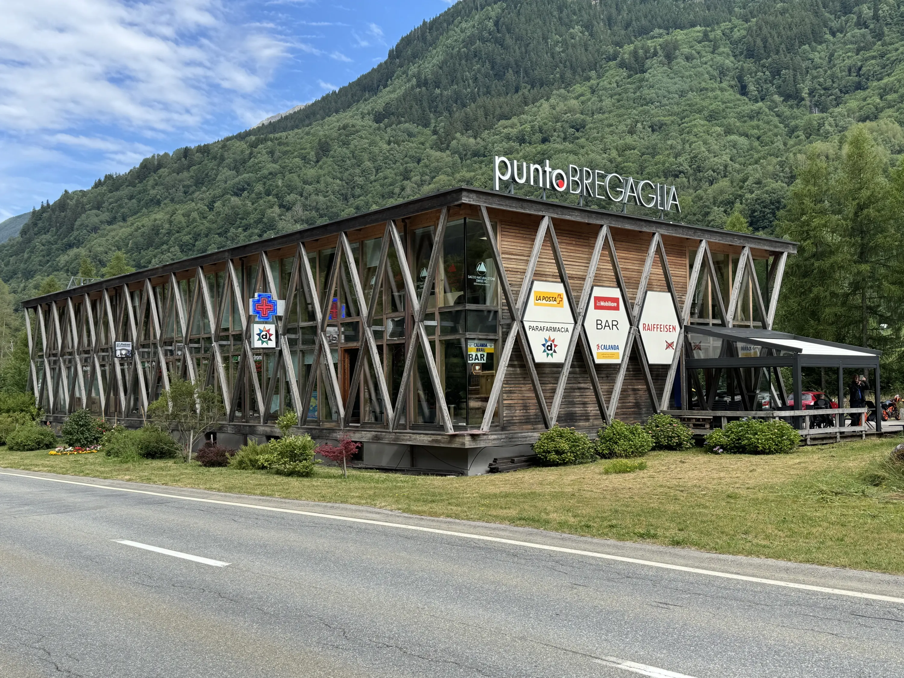 Un edificio moderno e stilizzato, con una facciata in legno e grandi finestre. Si trova in una zona montuosa, circondato da alberi e una strada. Diverse insegne pubblicitarie sono visibili all'esterno, indicando bar e servizi.