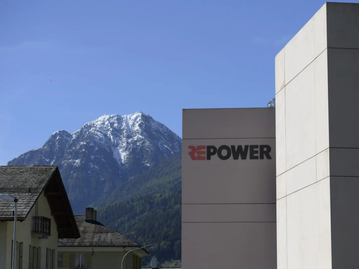 Edificio di Repower con un grande logo rosso su un fondale montano innevato e cielo sereno.