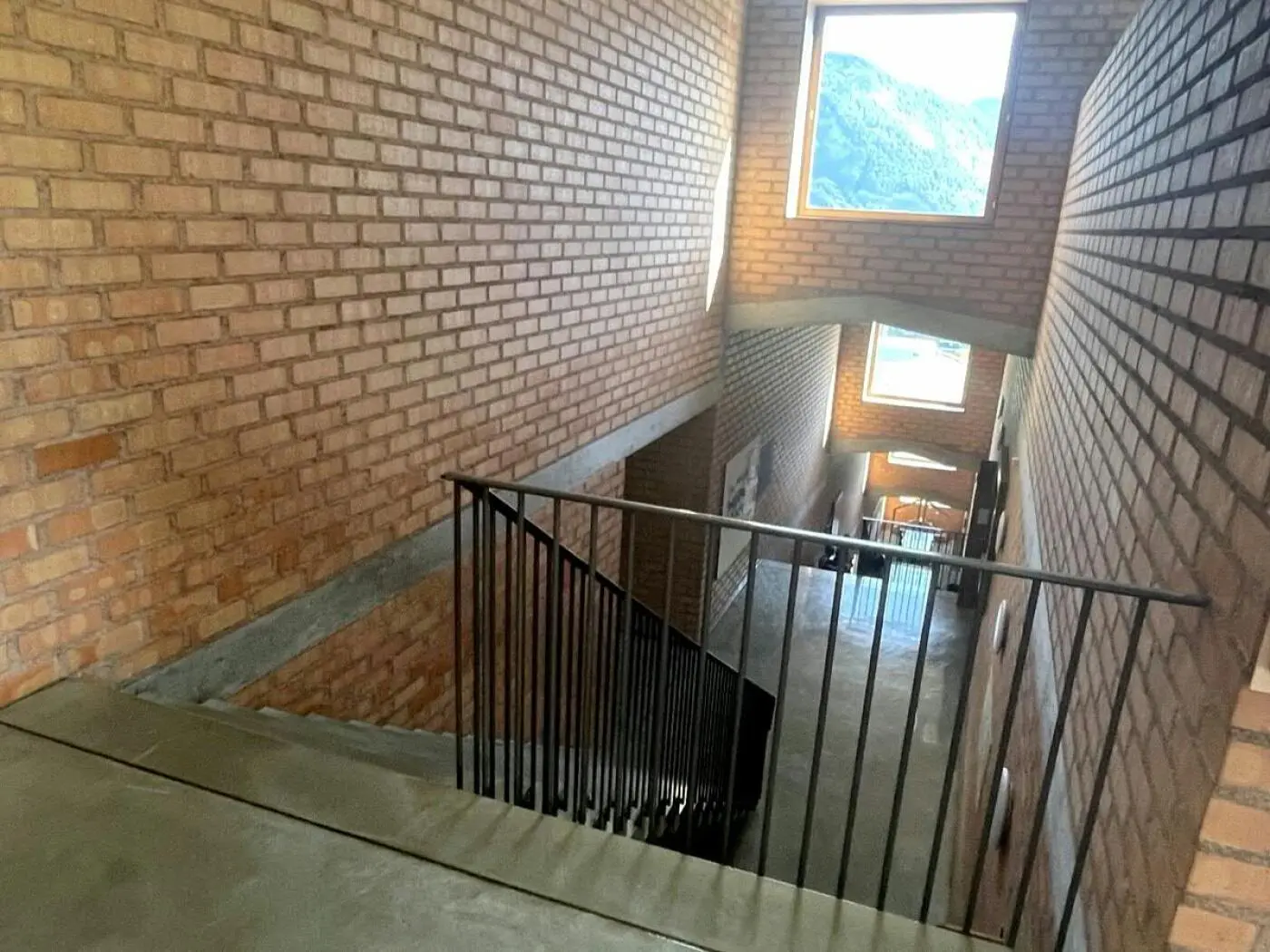Scala in un edificio con pareti in mattoni, vista dall'alto. La scala è circondata da finestre che illuminano l'ambiente. Il pavimento è in cemento.