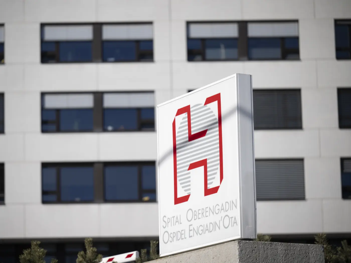 Insegna del Spital Oberengadin con il logo rosso e la scritta in tre lingue: "Spital Oberengadin", "Ospidel Engiadin'Ota". Sullo sfondo si intravede un edificio moderno con finestre.