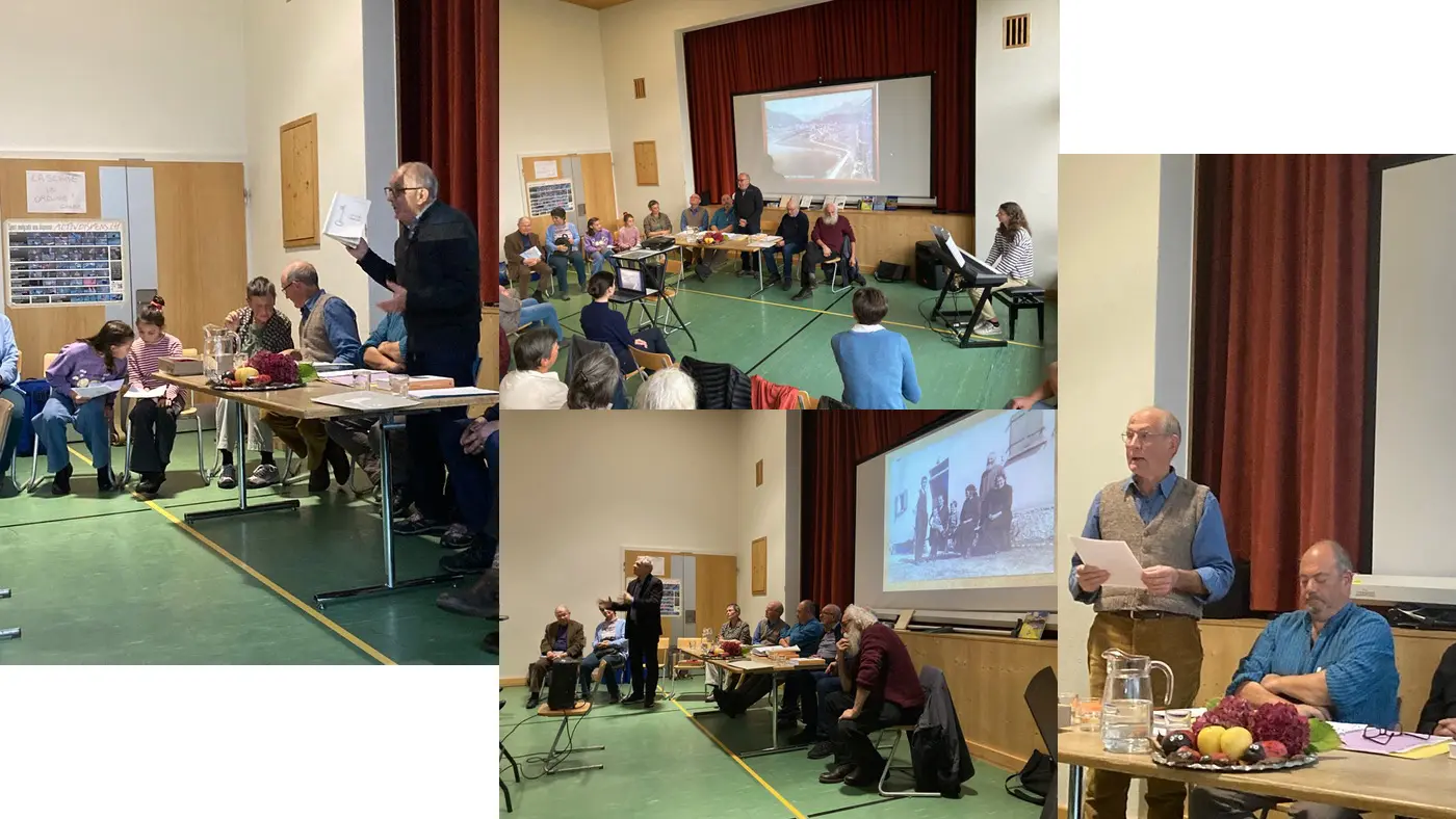 Un incontro in una sala, con una presentazione su uno schermo. Diverse persone sedute ai tavoli ascoltano, mentre un uomo in piedi legge un documento. Alcuni partecipanti prendono appunti, mentre altri guardano verso il relatore.