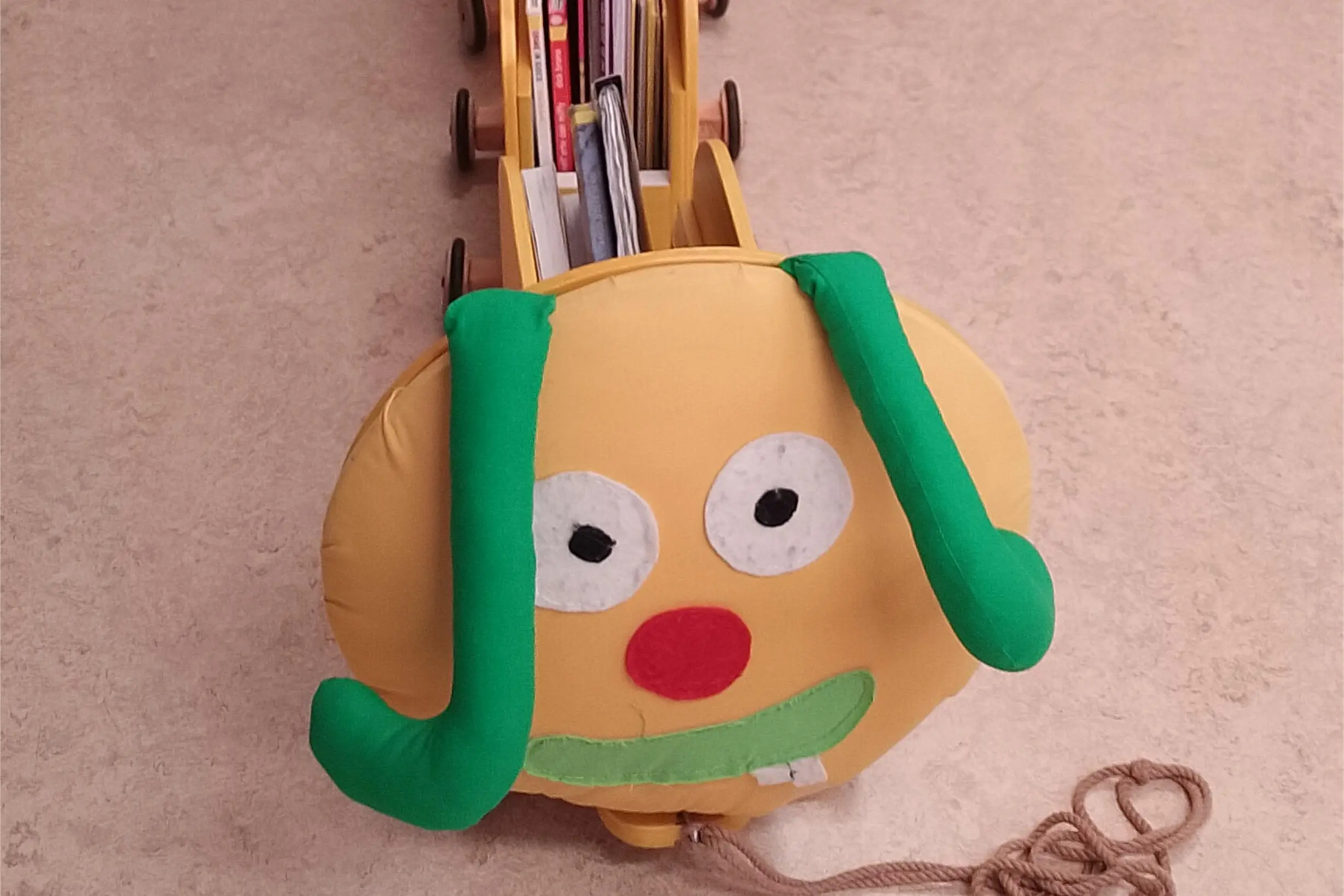 Un carrellino colorato a forma di insetto, con un grande viso giallo, occhi bianchi e un naso rosso. Ha lunghi ciuffi verdi e tiene dei libri all'interno.