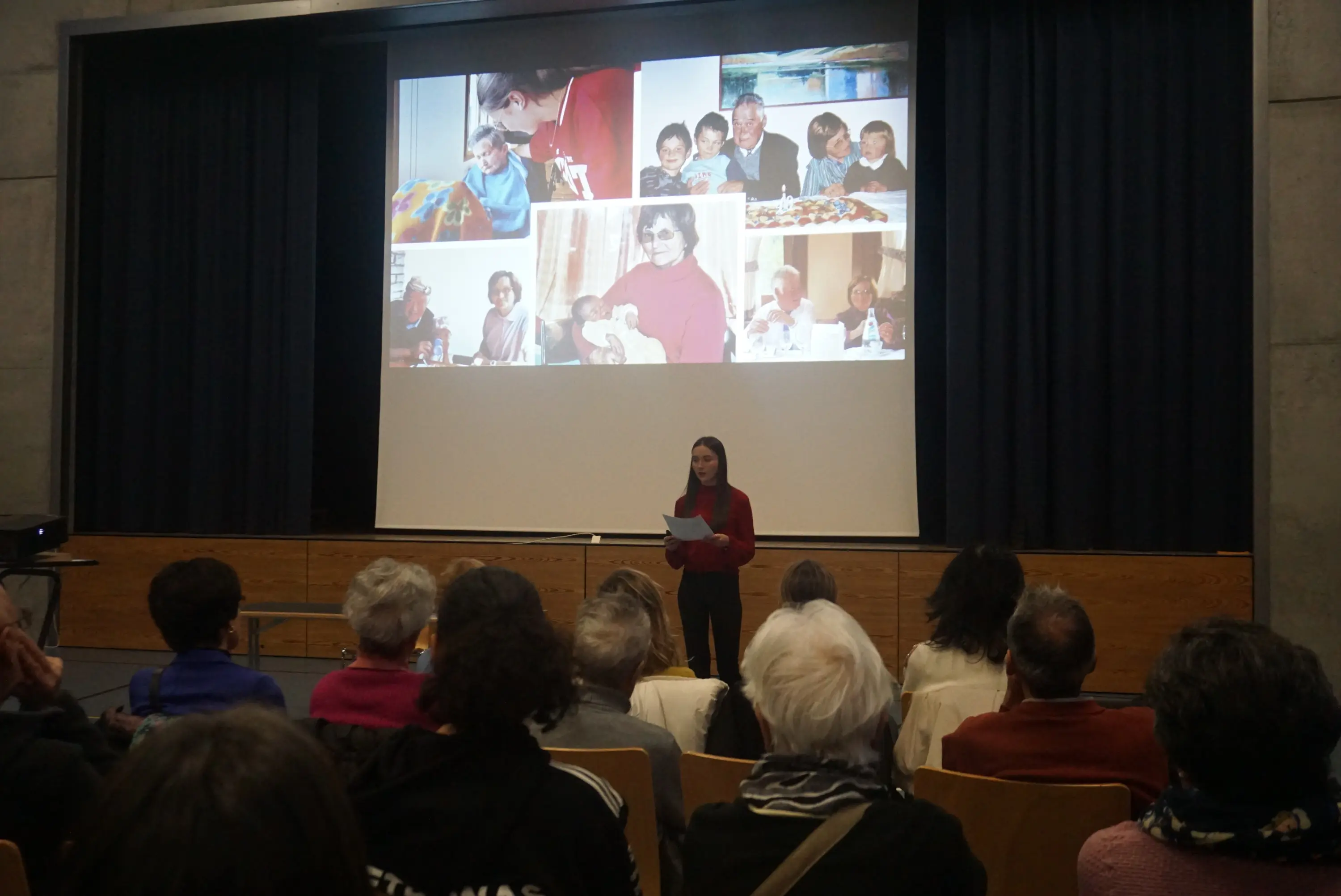 Una persona in piedi, che tiene un foglio, presenta davanti a un pubblico seduto. Sullo sfondo ci sono collage di foto che ritraggono momenti di interazione tra adulti e bambini durante eventi conviviali.