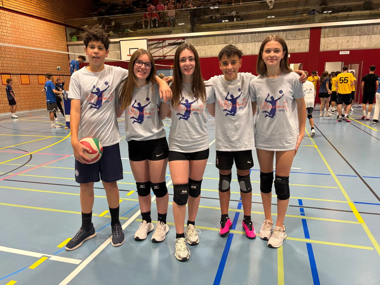 Cinque giovani atleti sorridenti indossano magliette grigie, pronti per una partita di pallavolo in un palazzetto.