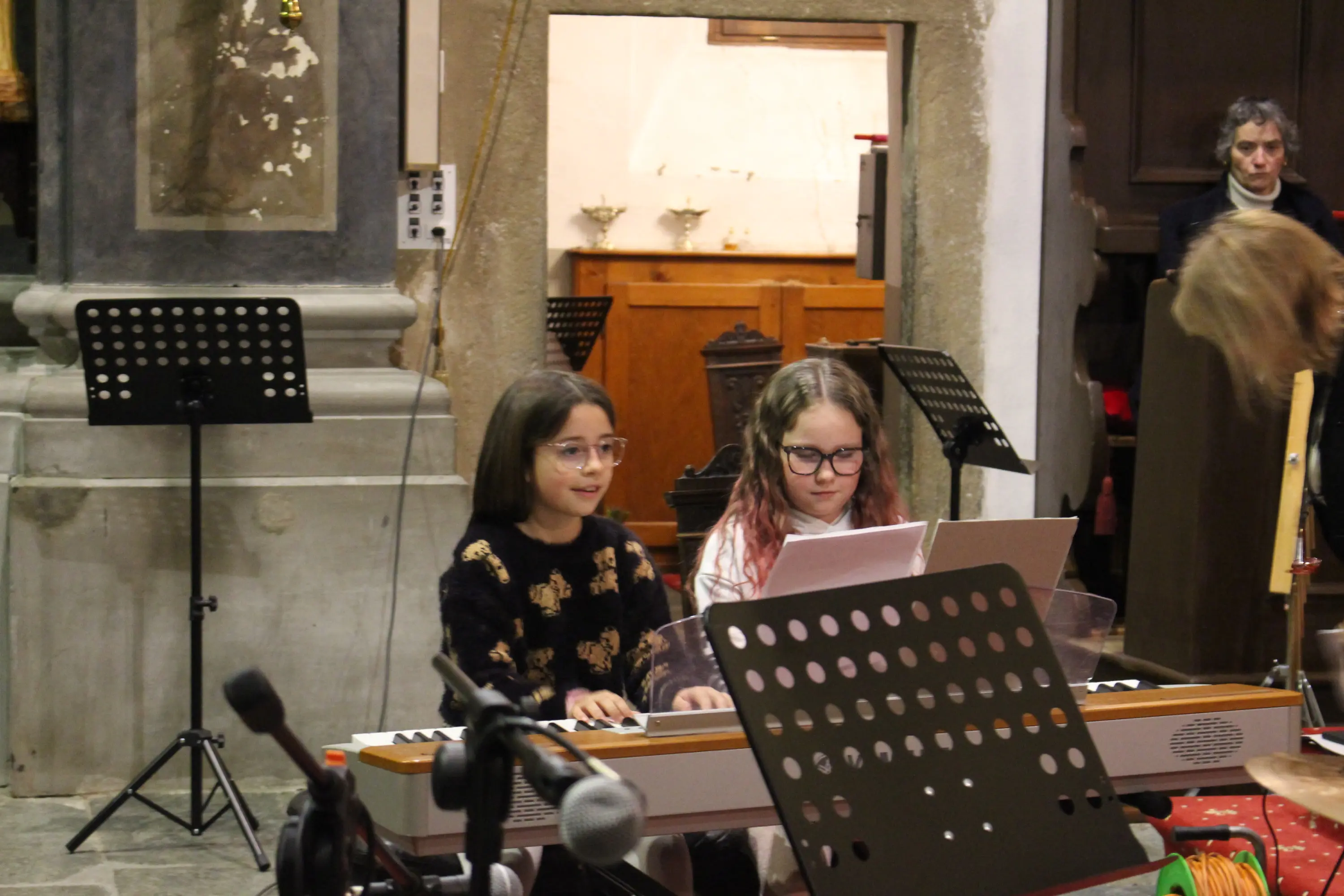 Due bambine suonano una tastiera in una chiesa. Una ragazza indossa occhiali e una maglietta scura con un motivo. L'altra è concentrata sul suo