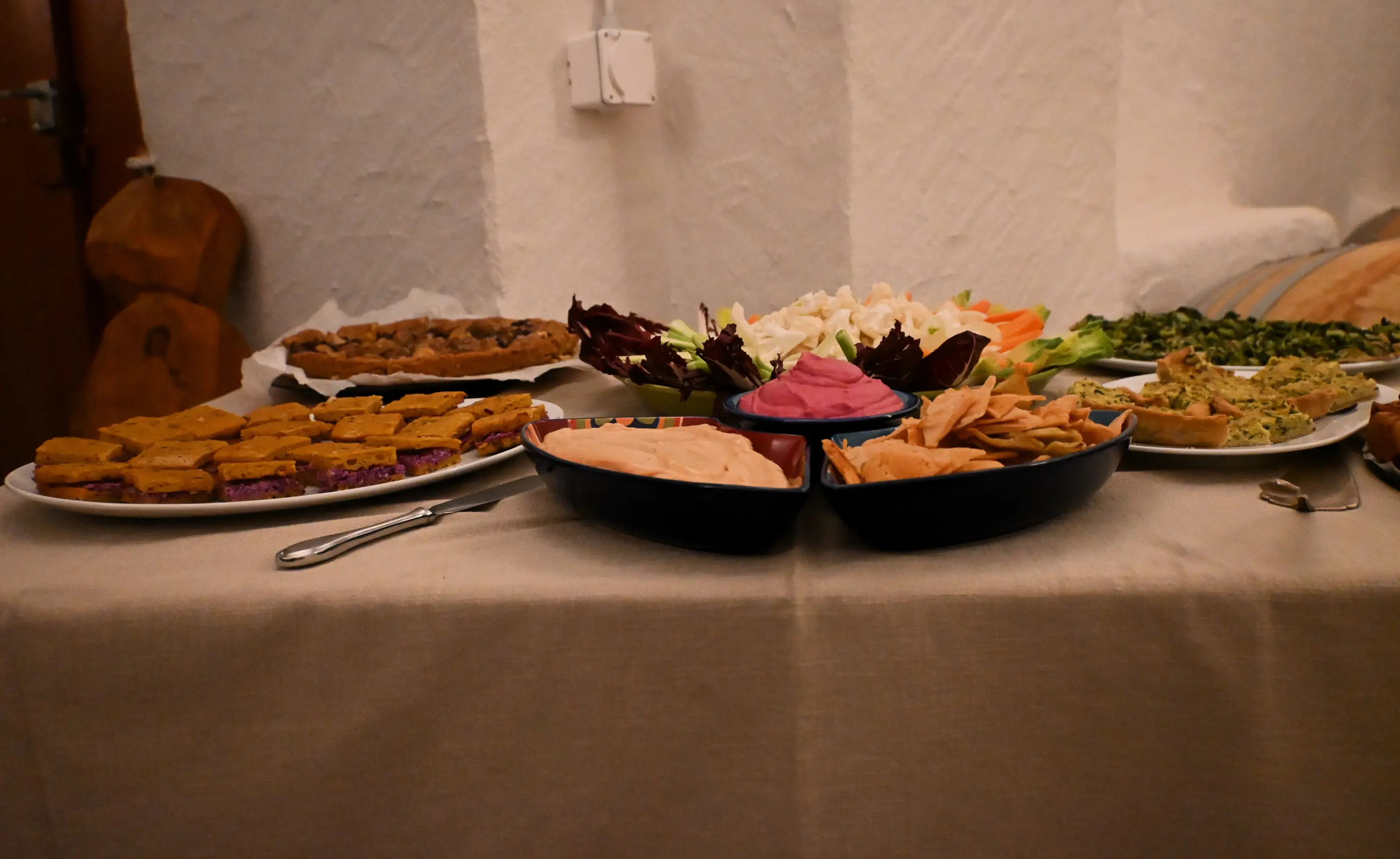 Un tavolo ricco di piatti assortiti, con diverse colorate dip e antipasti. Ci sono vaschette di hummus e altre creme, accompagnate da un assortimento di verd