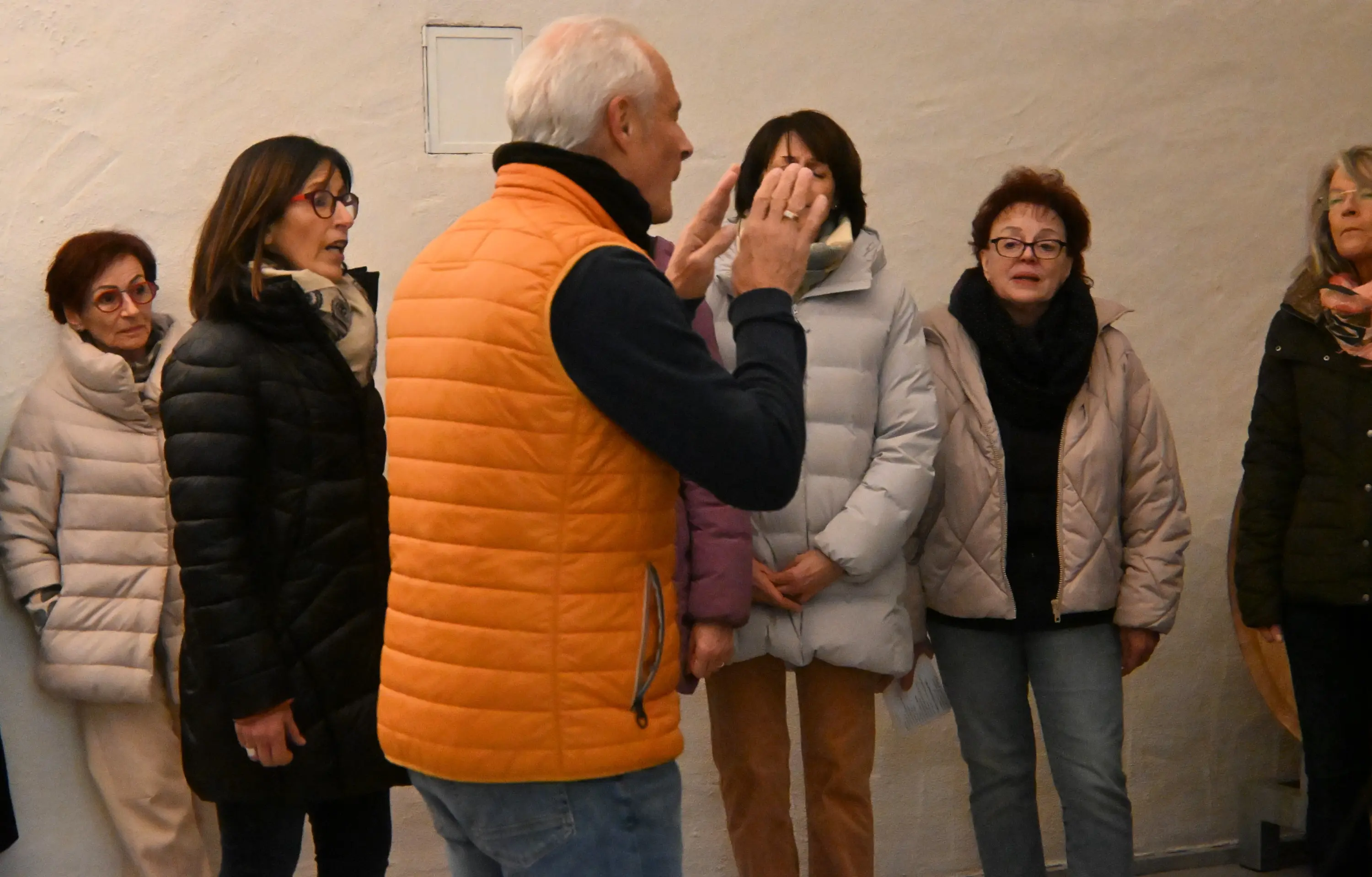 Un uomo con un gilet arancione sta parlando a un gruppo di sei donne vestite con giacche invernali. Le donne ascoltano attentamente mentre si trovano in