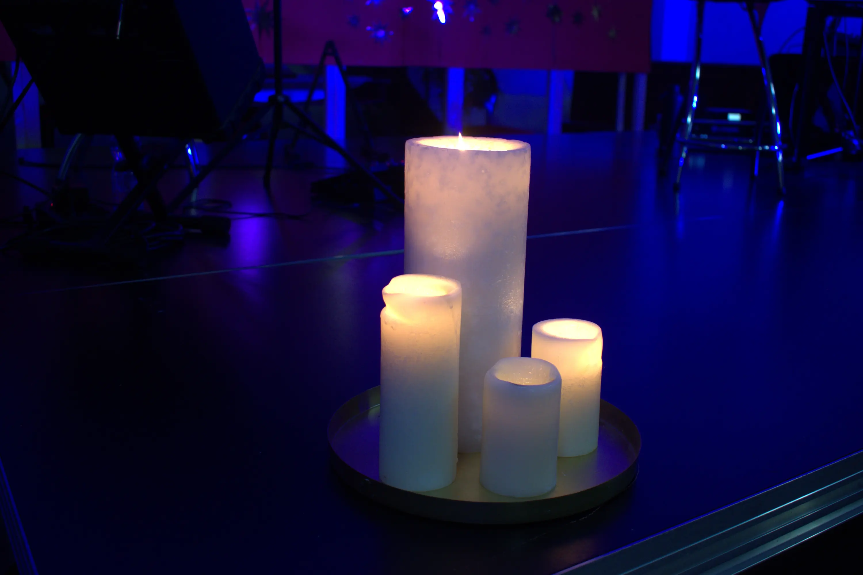 Candele accese di varie dimensioni su un vassoio, illuminate da una luce blu sullo sfondo.