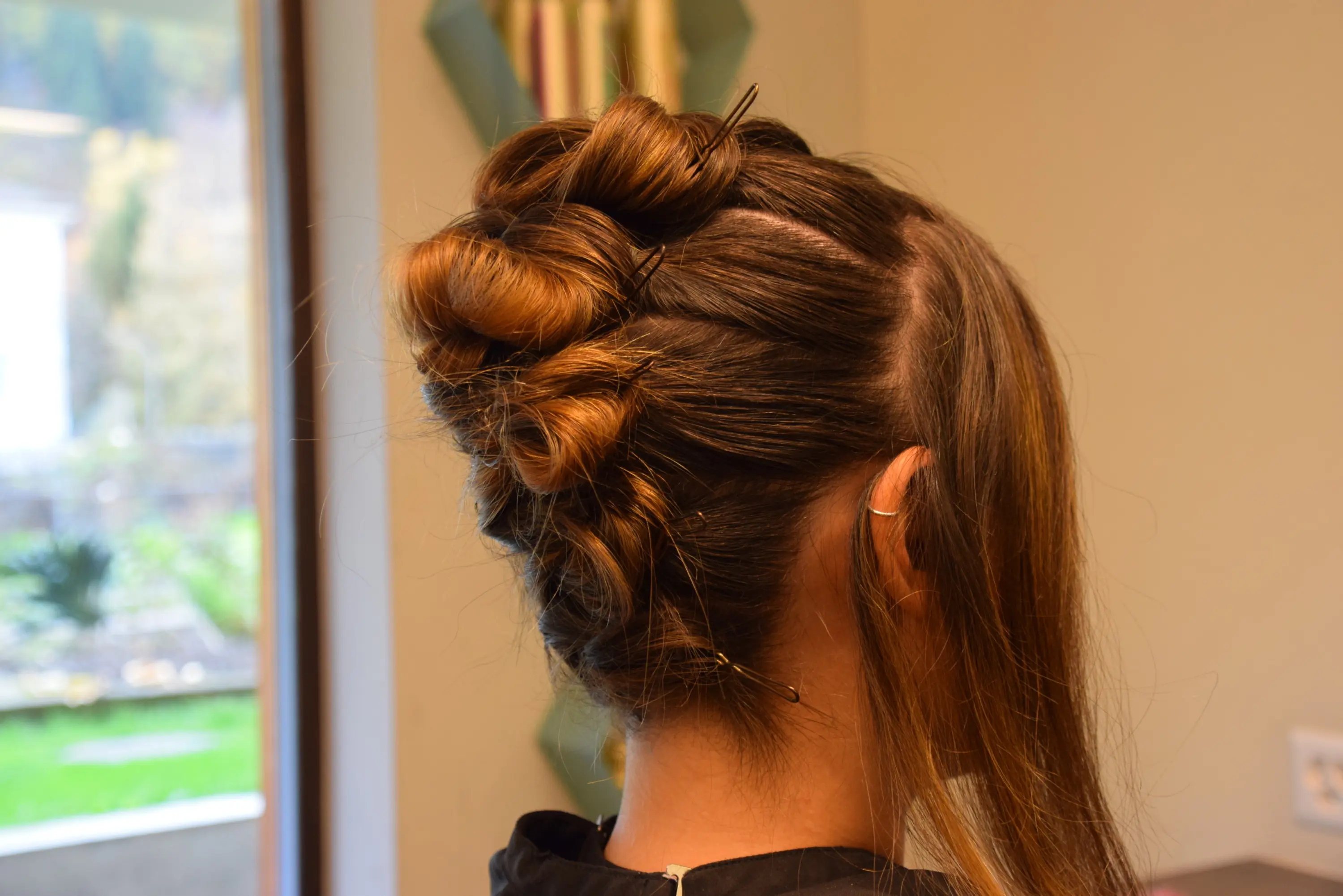 Acconciatura elegante con capelli raccolti in un bun creativo, con alcune ciocche sciolte.