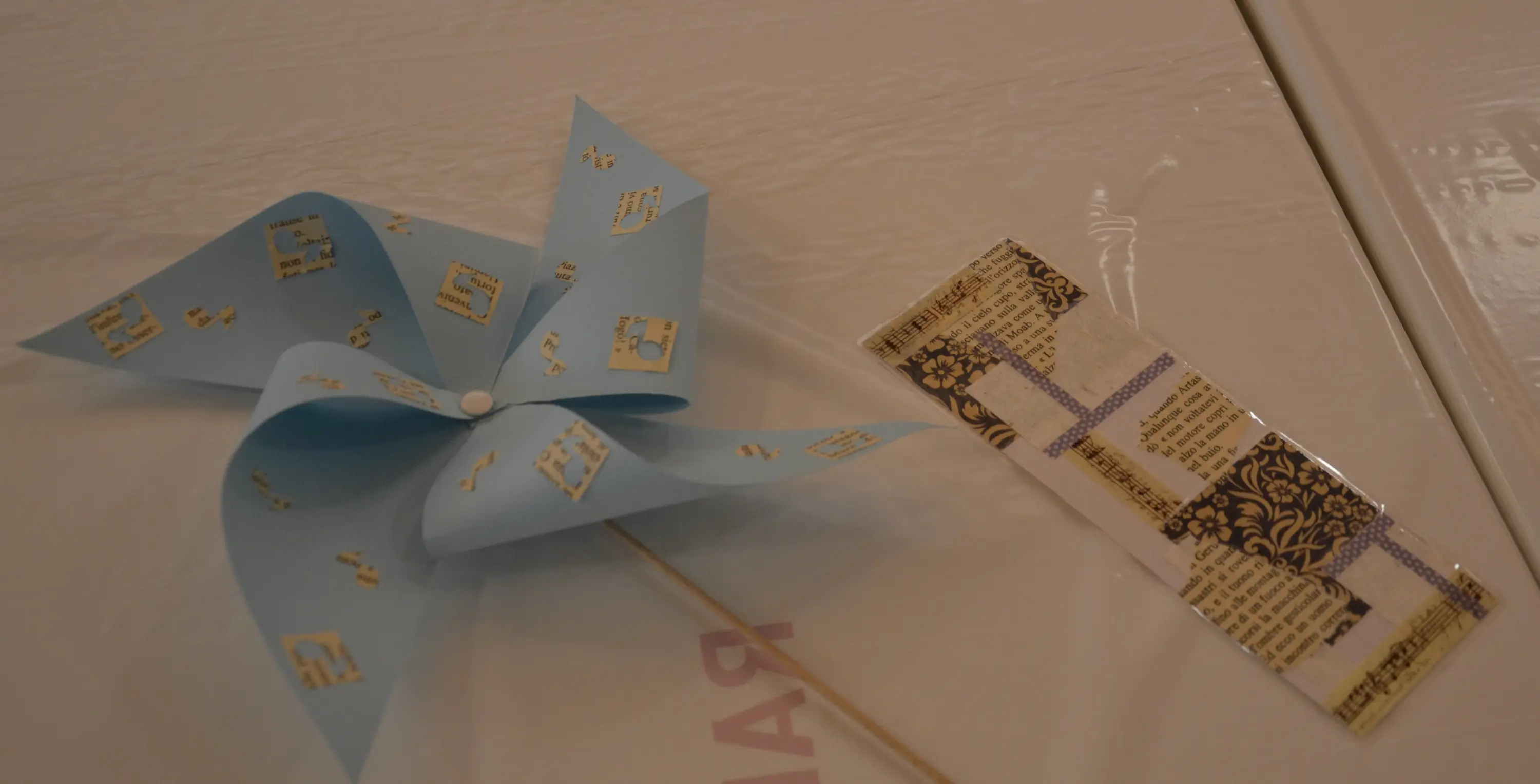 Un mulino di carta blu decorato con motivi dorati accanto a un segnalibro realizzato con ritagli di carta stampata in colori e design diversi.