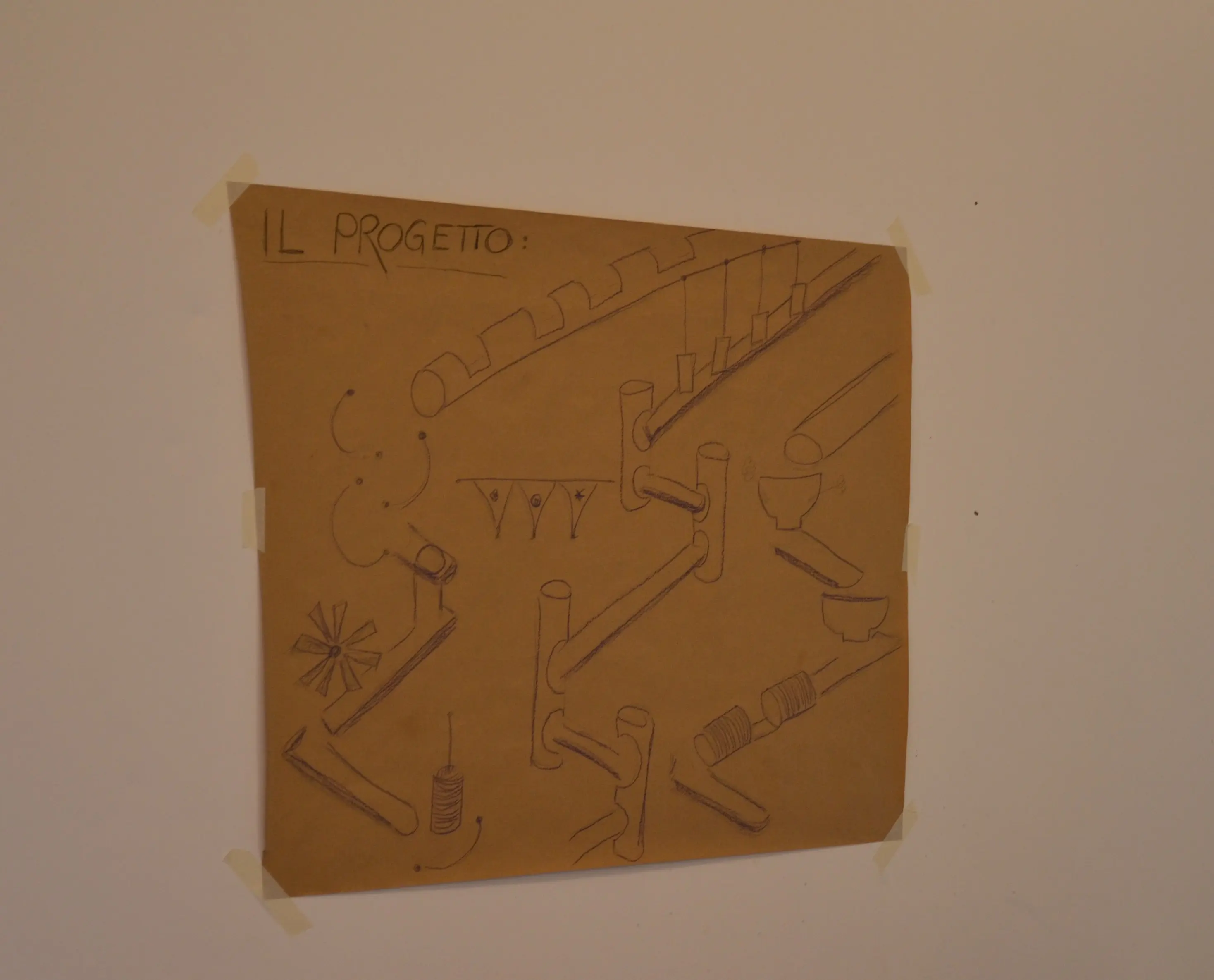 Disegno tecnico appeso a una parete, con diverse illustrazioni di tubazioni e raccordi. In alto è scritto "Il progetto".