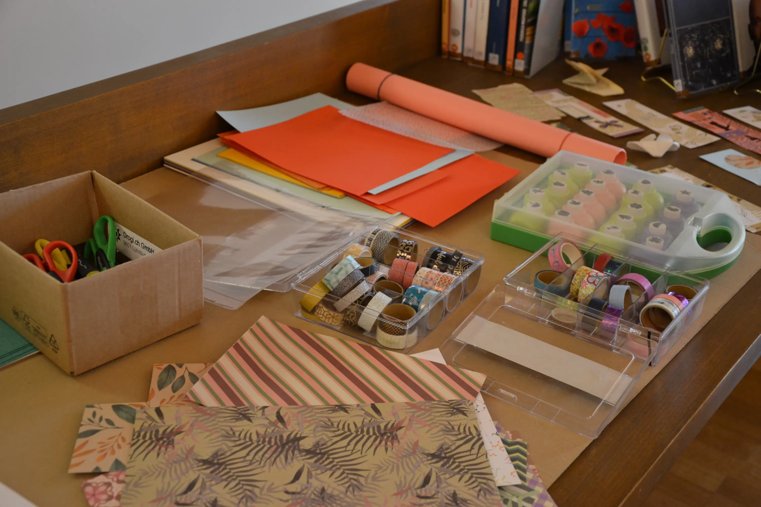 Una vista di un tavolo disordinato con materiali per il fai-da-te, inclusi fogli colorati, forbici, nastro adesivo, washi tape e scatole.