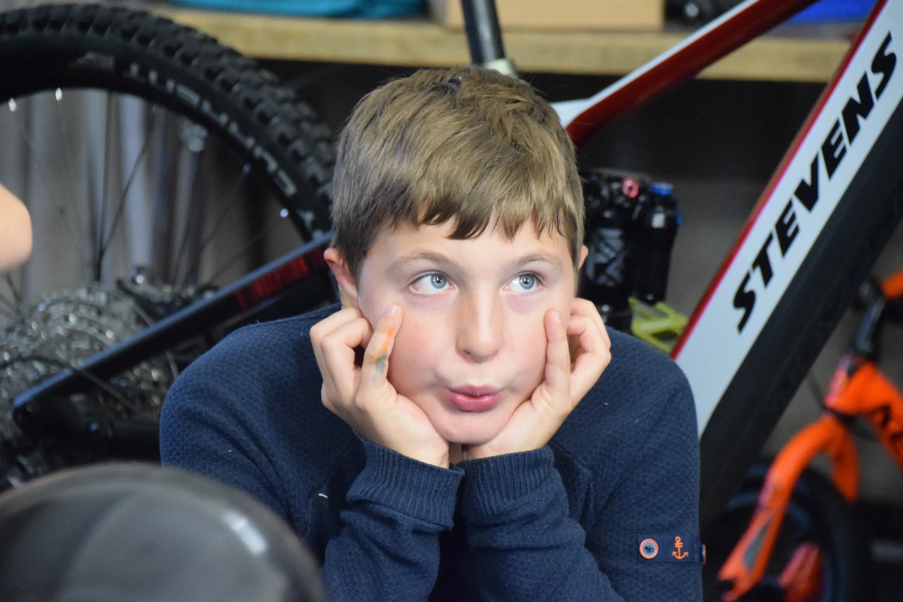 Un ragazzo con i capelli castani chiari, seduto con le mani sul viso e un'espressione pensierosa. Sullo sfondo si vedono delle biciclette.