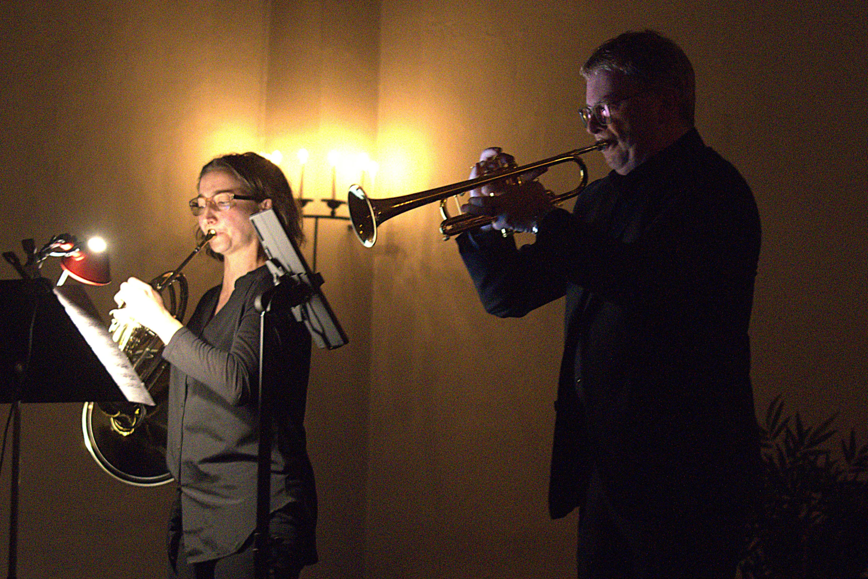 Due musicisti si esibiscono su un palco illuminato debolmente. Una musicista suona un corno francese mentre l'altro suona una tromba, entrambi concentrati