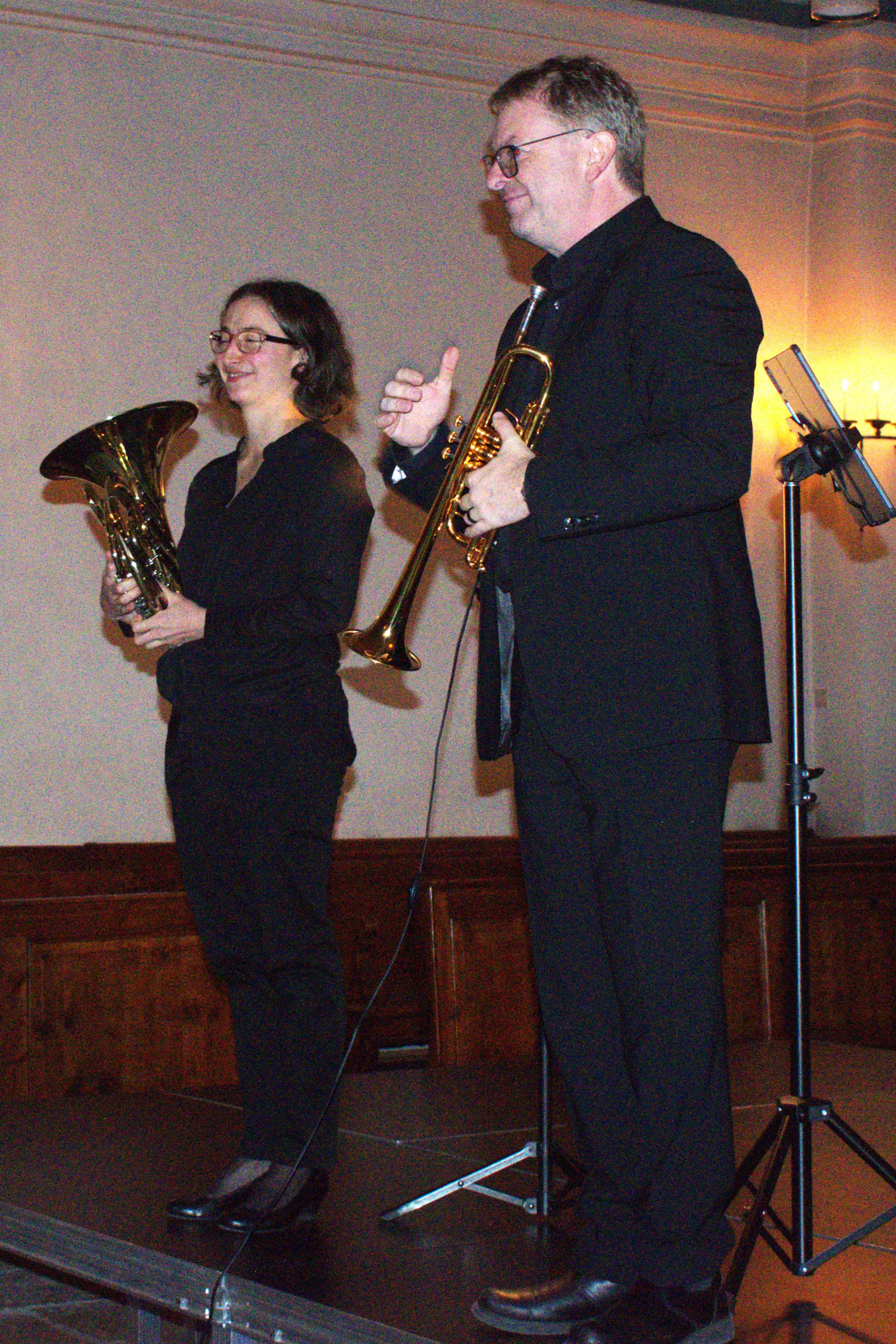 Due musicisti sul palco. Una donna sorregge un'eufonio mentre un uomo tiene una tromba. Entrambi indossano abiti neri e sorridono mentre si prepar