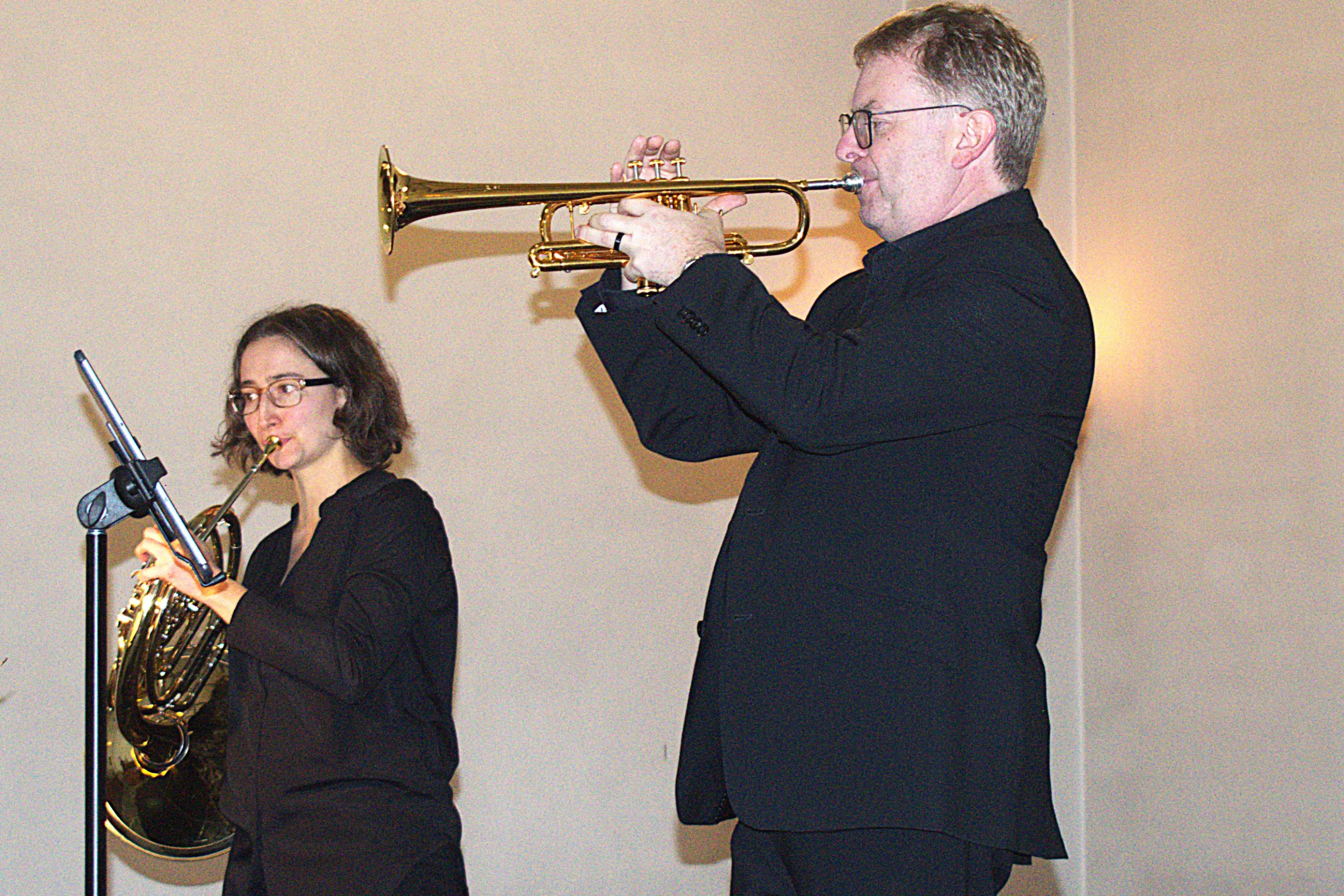 Due musicisti si esibiscono: un uomo con una tromba e una donna con una tuba, entrambi indossano abbigliamento nero.