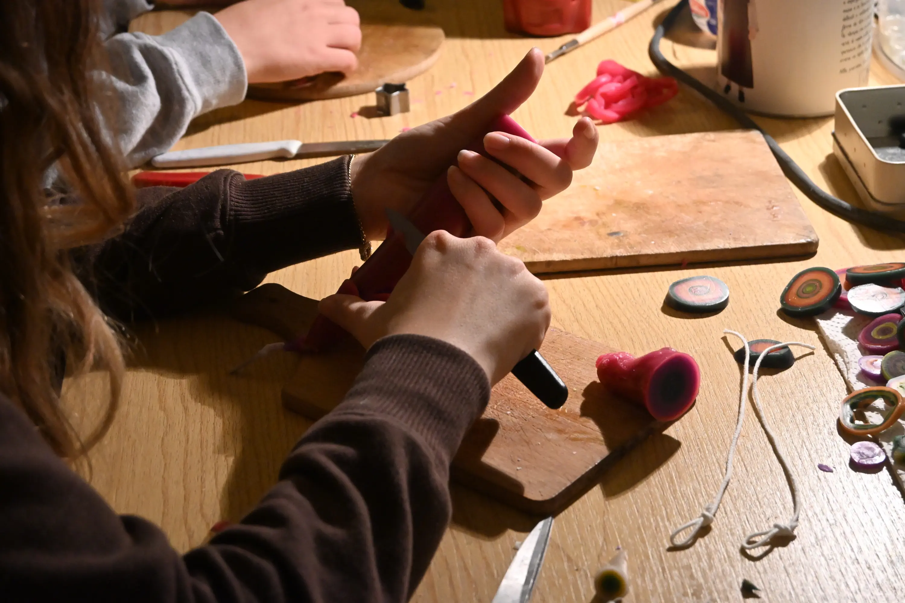 Mani che lavorano su un pezzo di pasta modellabile, con vari strumenti e decorazioni colorate sparsi su un tavolo di legno.