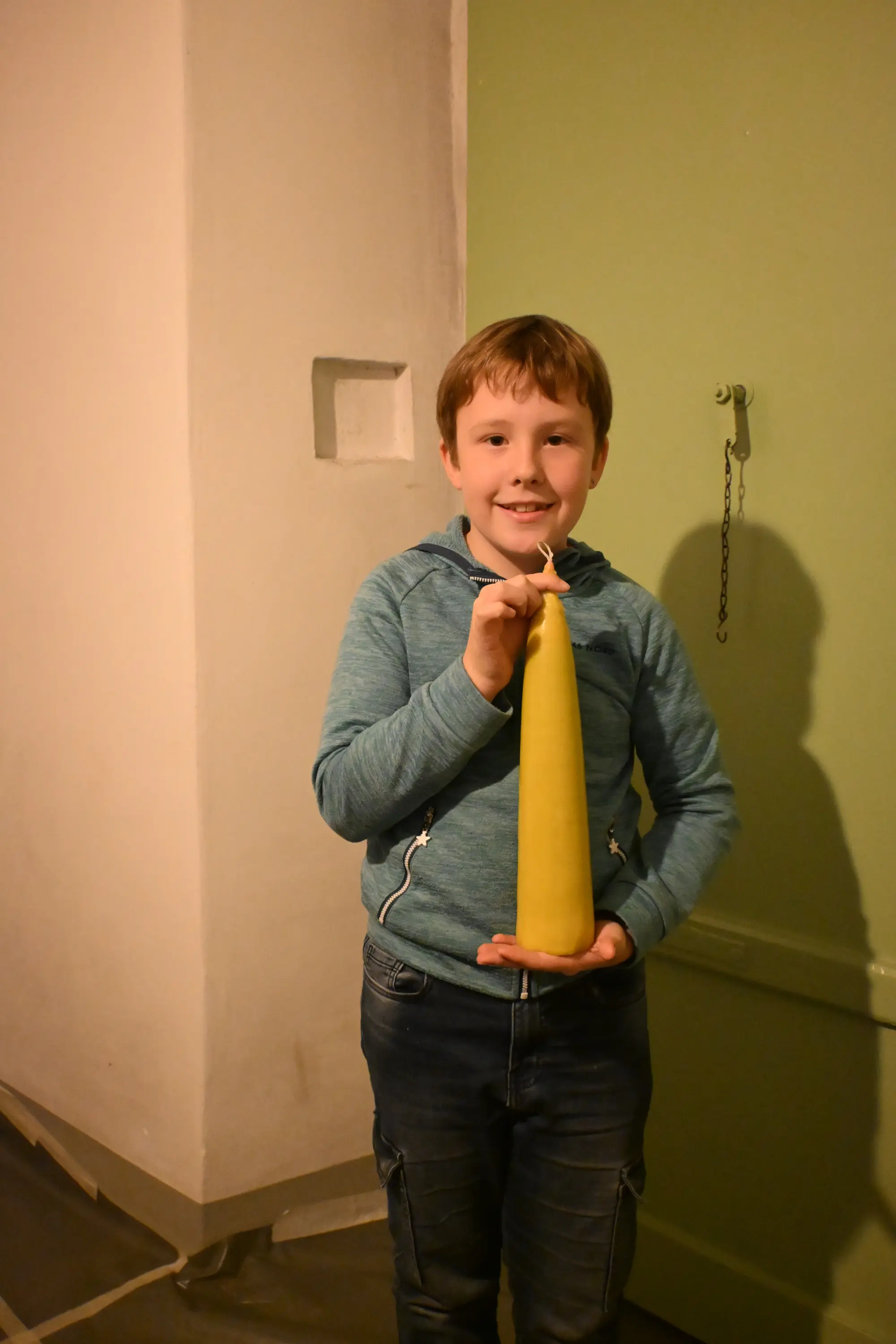 Ragazzo sorridente tiene in mano una candela gialla, con un muro verde sullo sfondo.