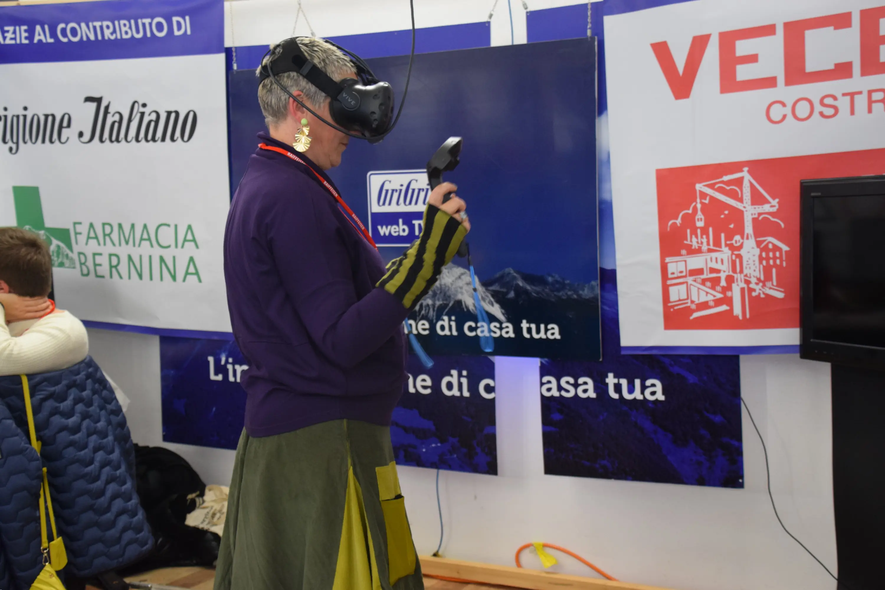 Una persona indossa un visore VR e tiene un controller mentre interagisce con un ambiente virtuale. Sullo sfondo si vedono vari cartelloni pubblicitari.
