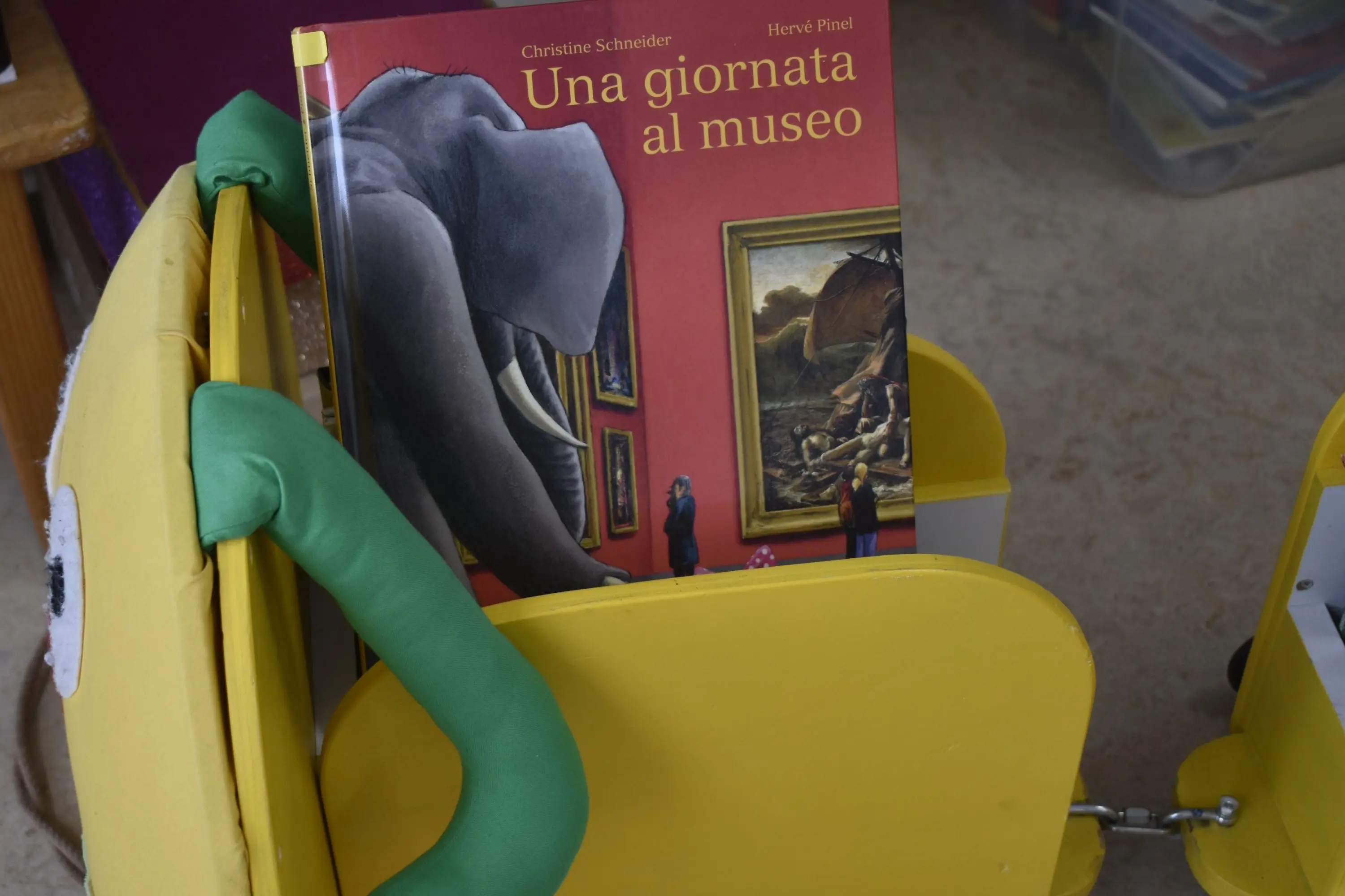 Un libro intitolato "Una giornata al museo" con la copertina che mostra un elefante, posizionato su un seggiolino giallo.