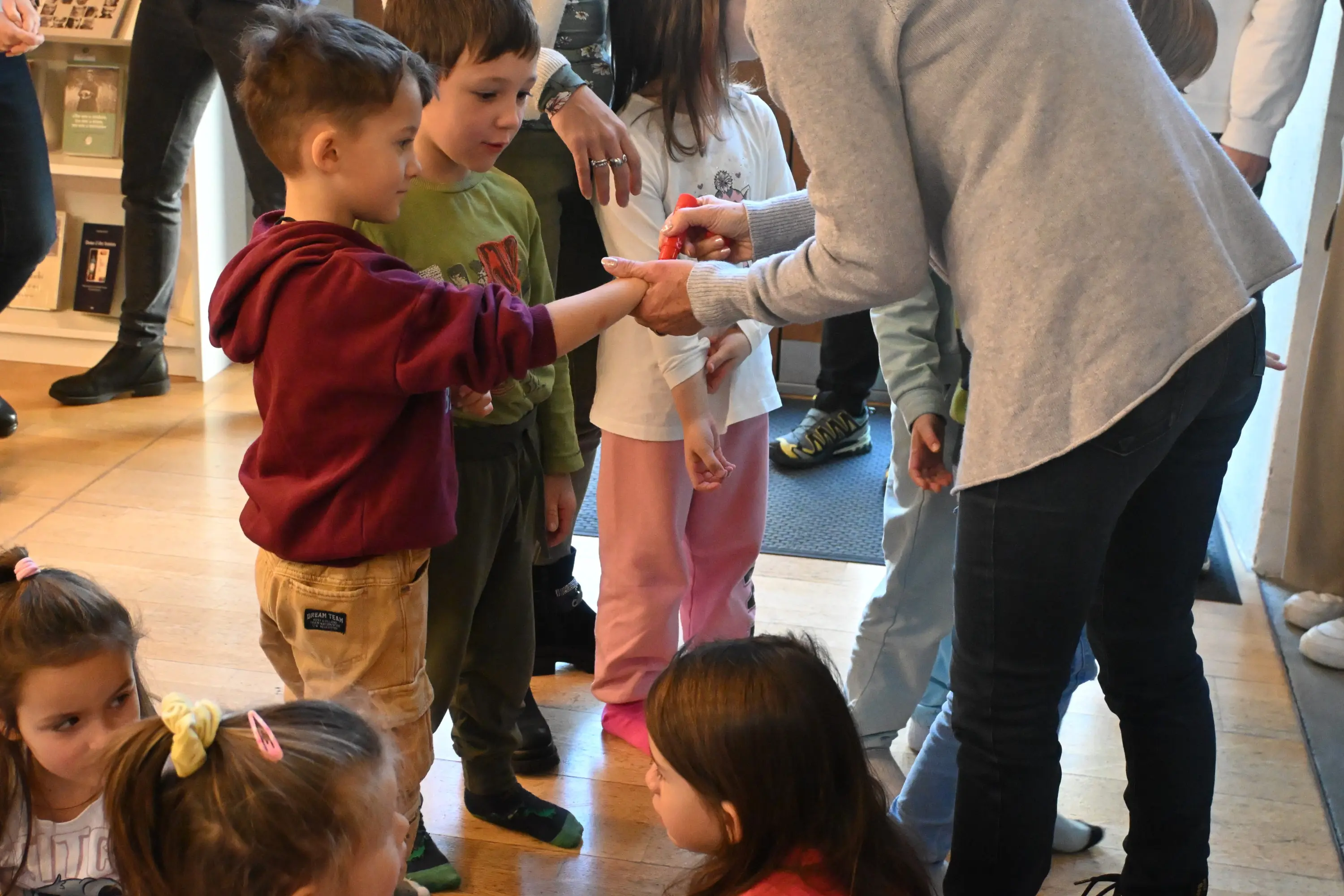 Un gruppo di bambini si riunisce intorno a un adulto che mostra loro un'attività, con espressioni curiose e interessate.