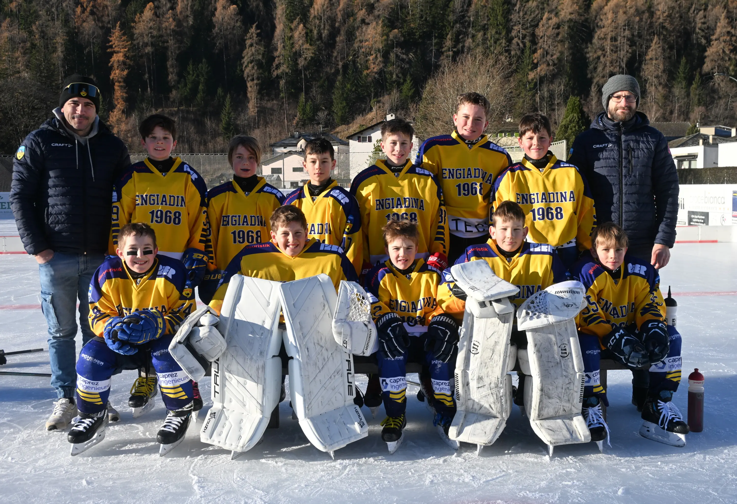 Una squadra di giovani hockeisti in divisa gialla e blu, composta da dodici ragazzi e due adulti, posano sorridenti su un campo di ghiaccio. Sullo sf