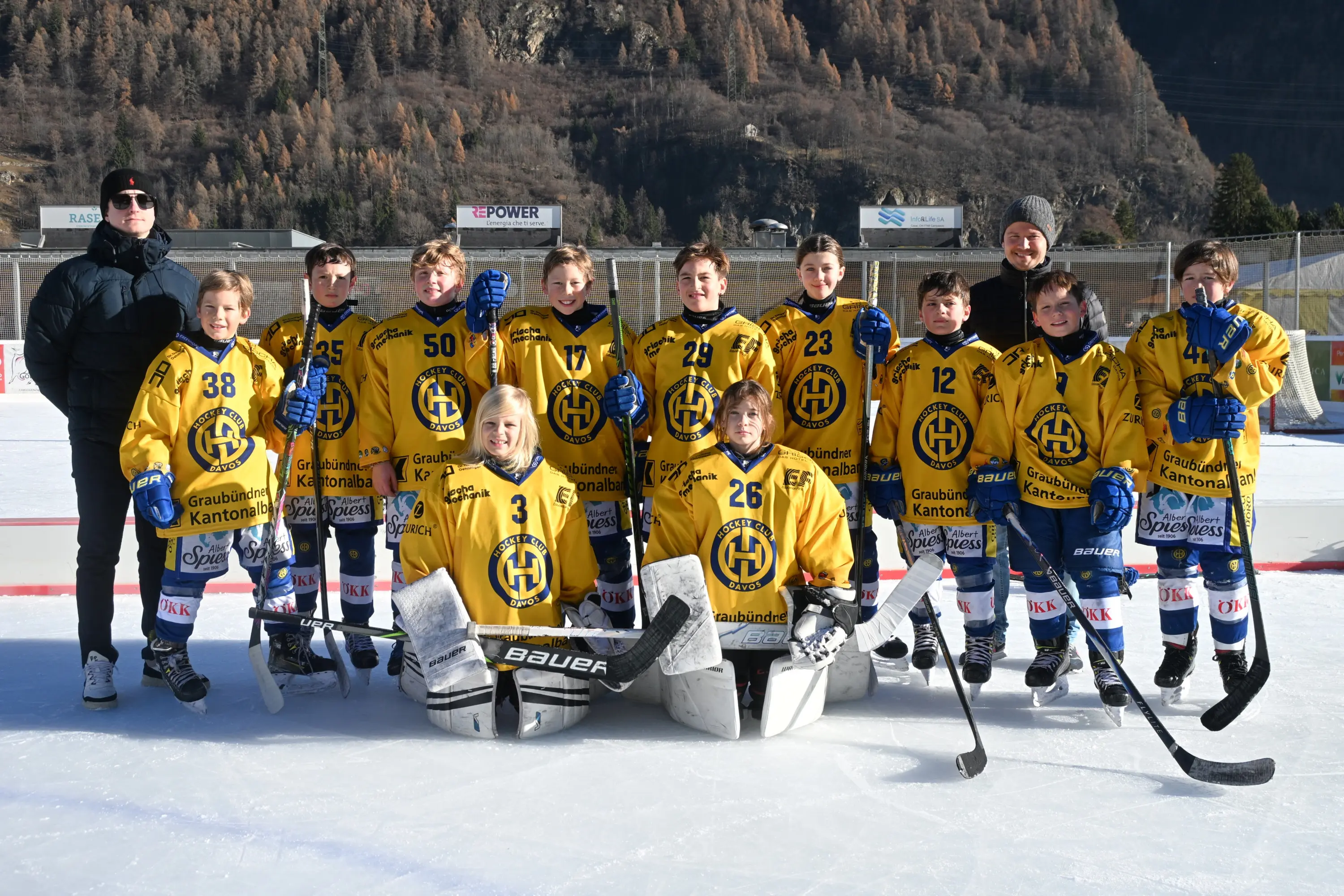 Gruppo di giovani giocatori di hockey su ghiaccio in maglia gialla con il logo della squadra, posano sorridendo su un campo di ghiaccio. Sono in 12, tra