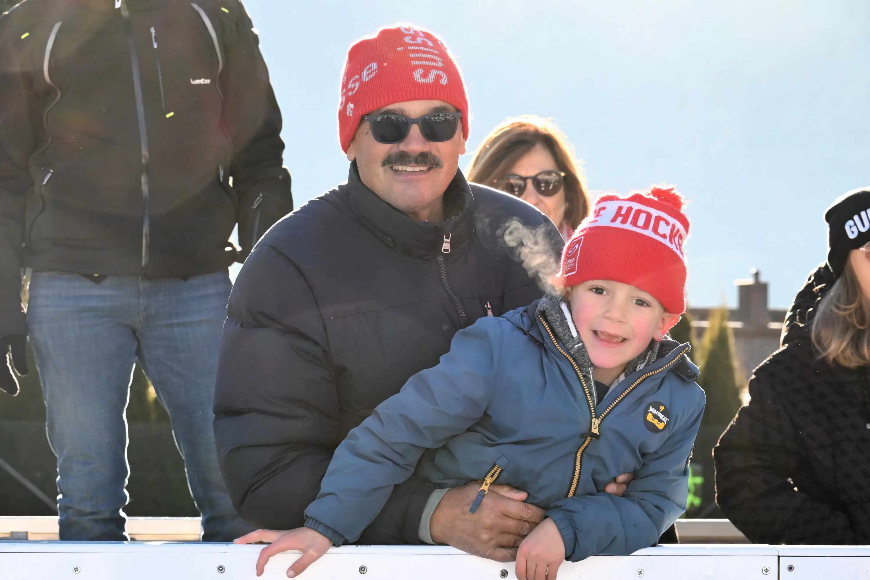 Uomo sorridente con un berretto rosso e bambino accanto a lui, entrambi felici e all'aperto in un ambiente innevato.