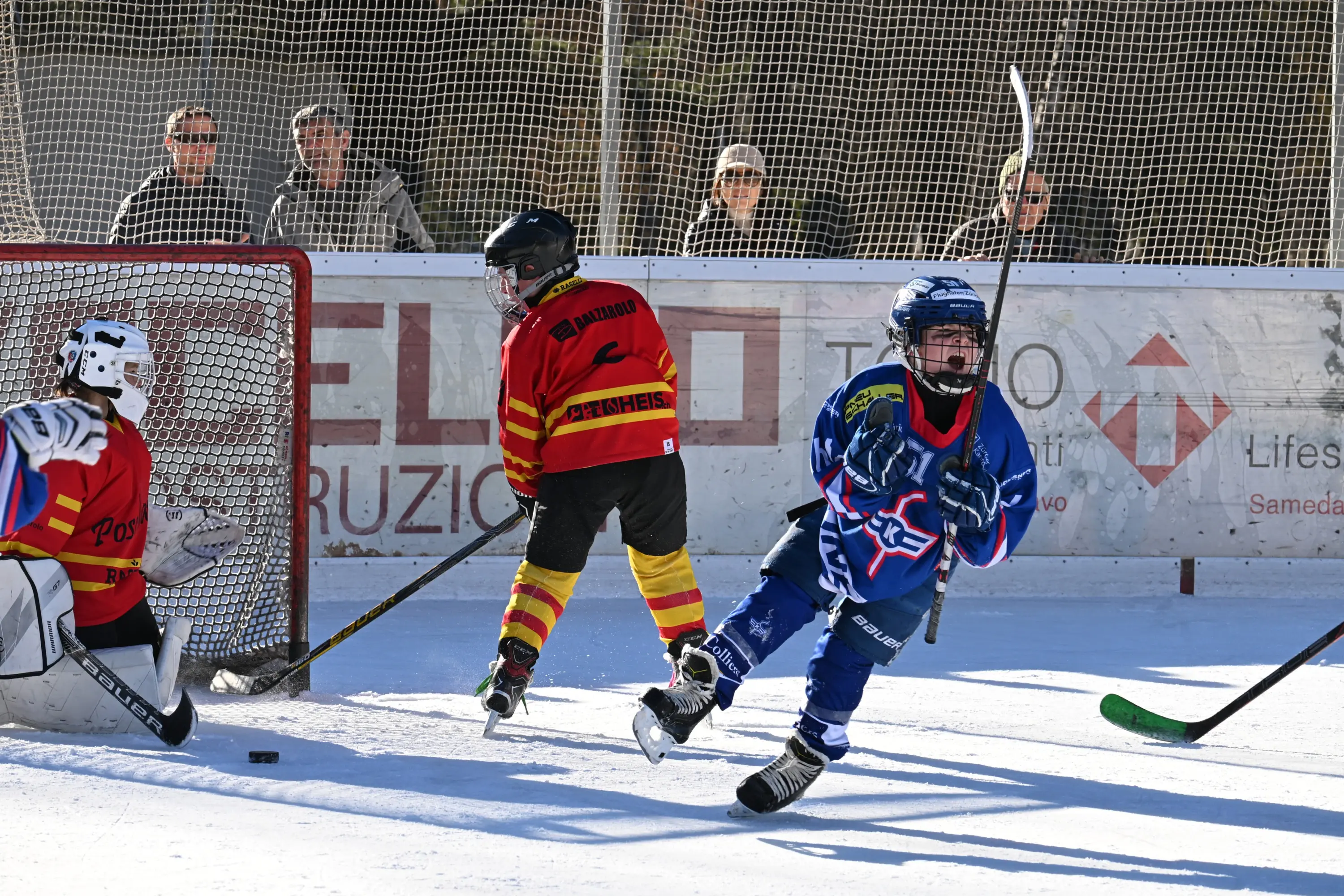 Giocatori di hockey su ghiaccio in azione su un campo all'aperto. Un giovane giocatore in maglia blu festeggia un gol, mentre un avversario in maglia
