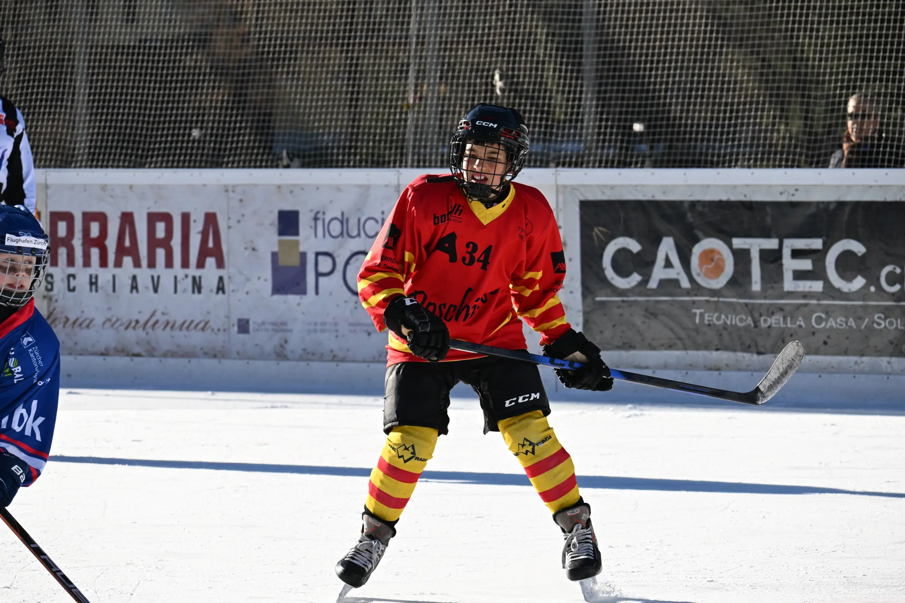 Giocatore di hockey su ghiaccio in divisa rossa e gialla, con bastone in mano, in azione su un campo di ghiaccio.