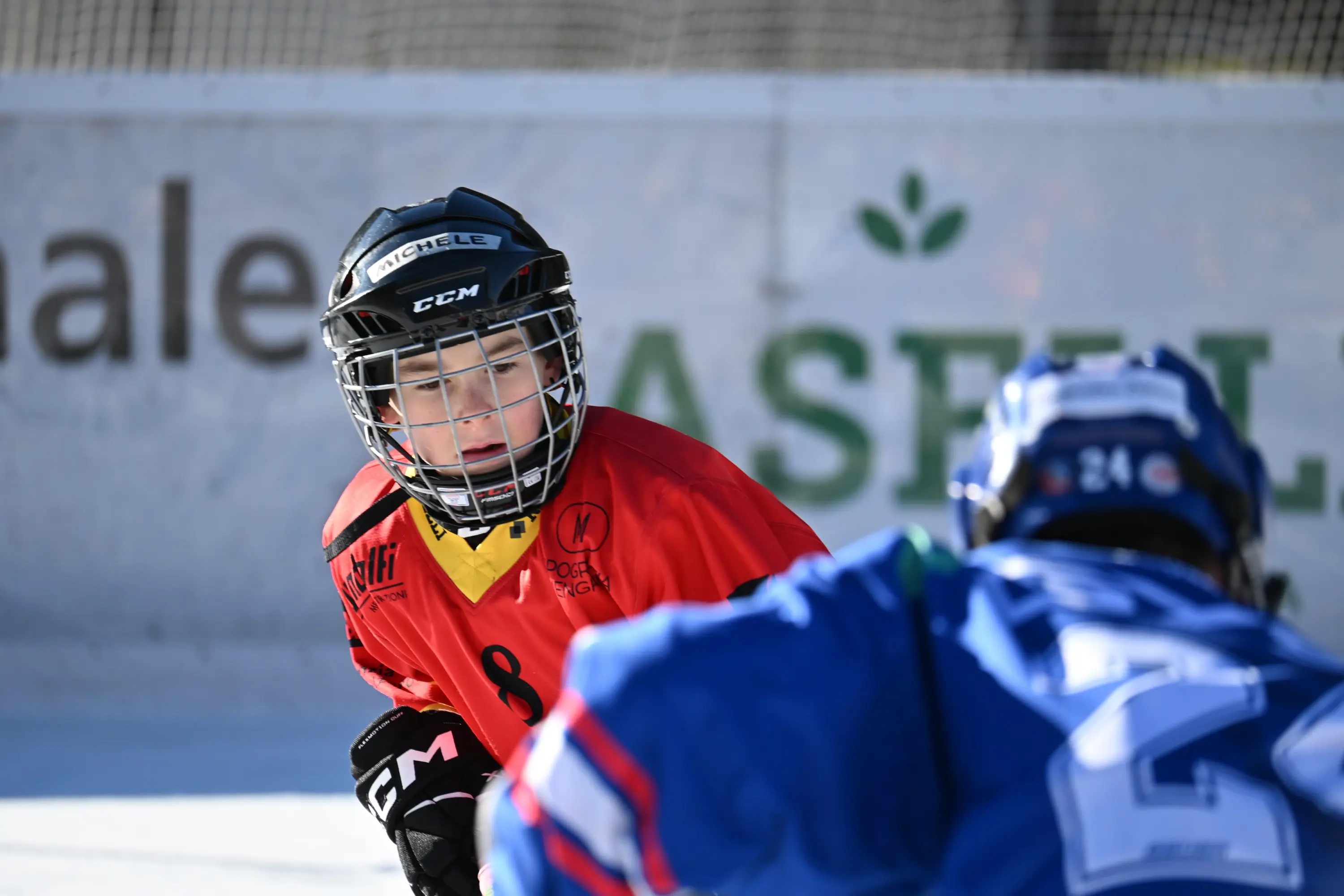 Giocatori di hockey su ghiaccio in azione, uno indossa una maglia rossa con il numero 8, l'altro una maglia blu. Il giocatore in rosso