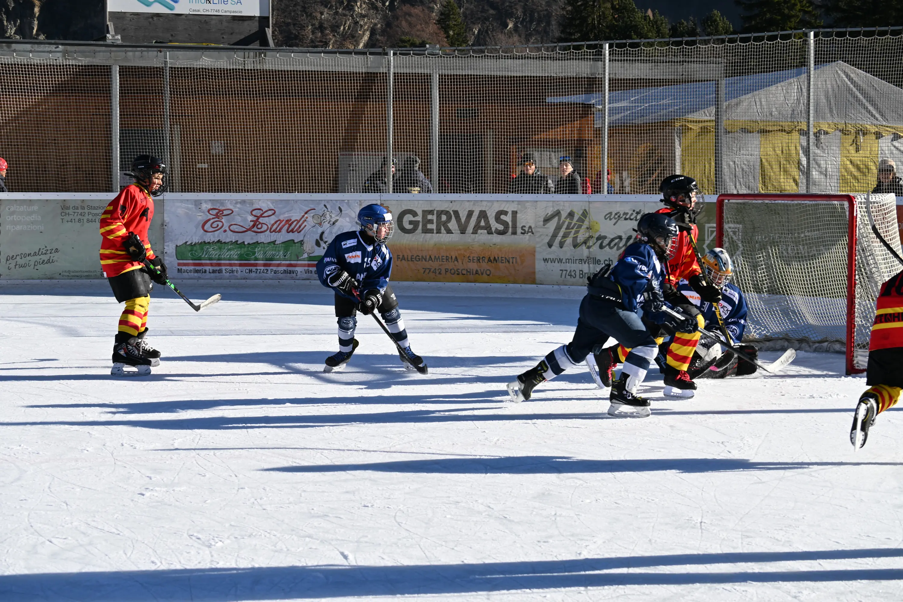 Giovani giocatori di hockey su ghiaccio in azione su un campo all'aperto. Due squadre, una con maglie blu e l'altra con maglie rosse e gialle