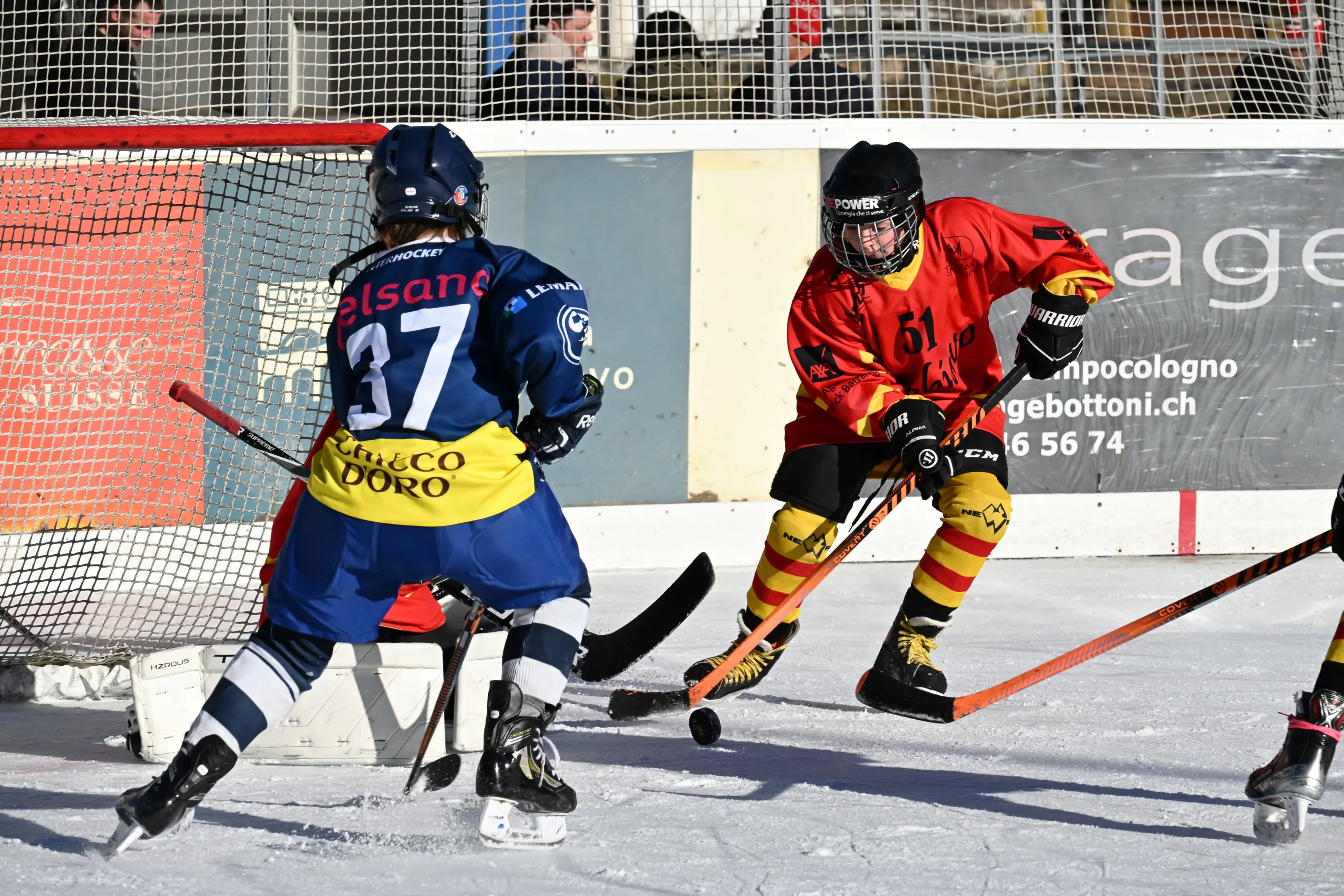 Giocatori di hockey su ghiaccio in azione, uno in maglia rossa con il numero 61 e l'altro in maglia blu con il numero 37, mentre manov