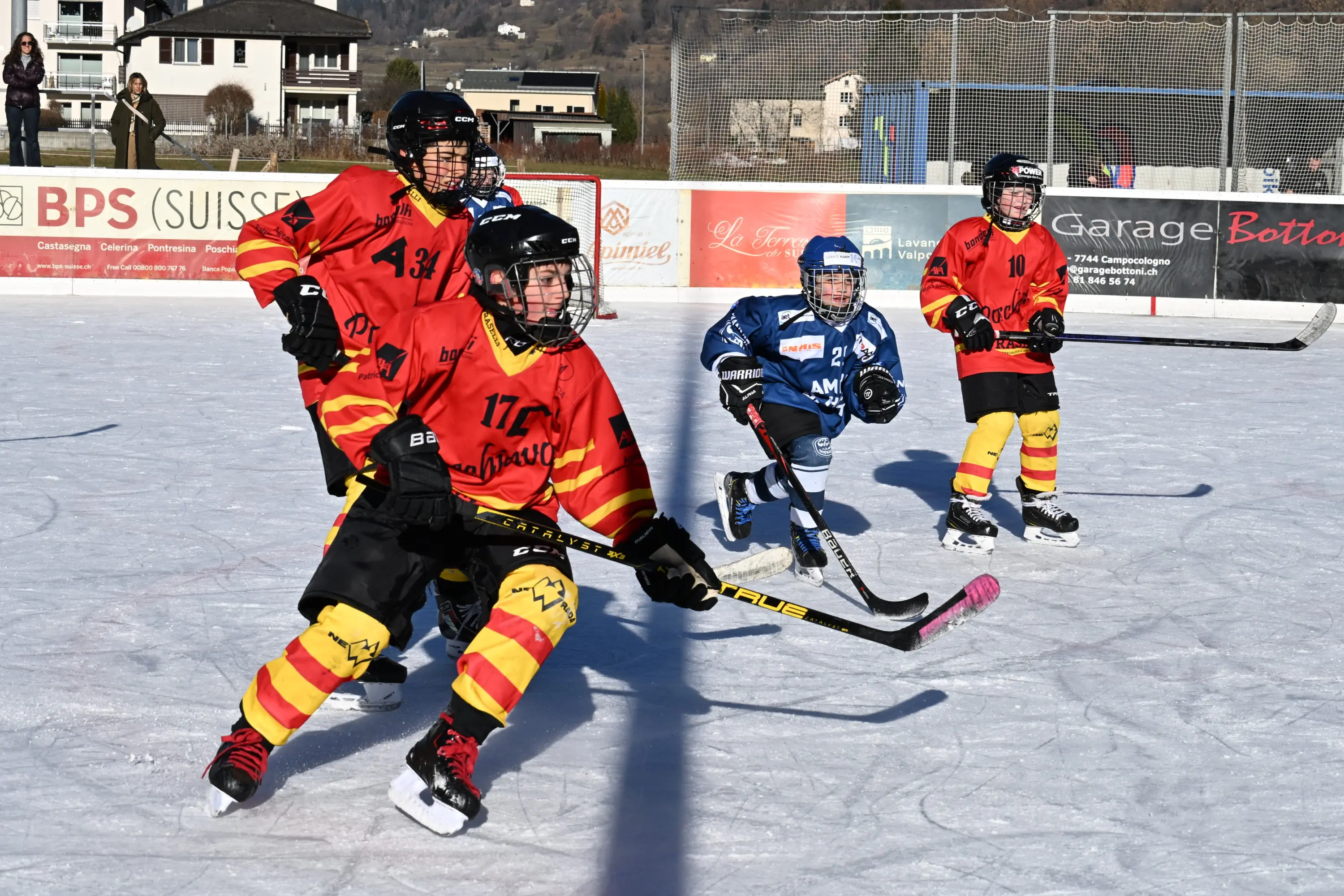 Giovani hockeisti stanno giocando su un campo ghiacciato. Due giocatori indossano maglie rosse e gialle mentre cercano di strappare il disco a un
