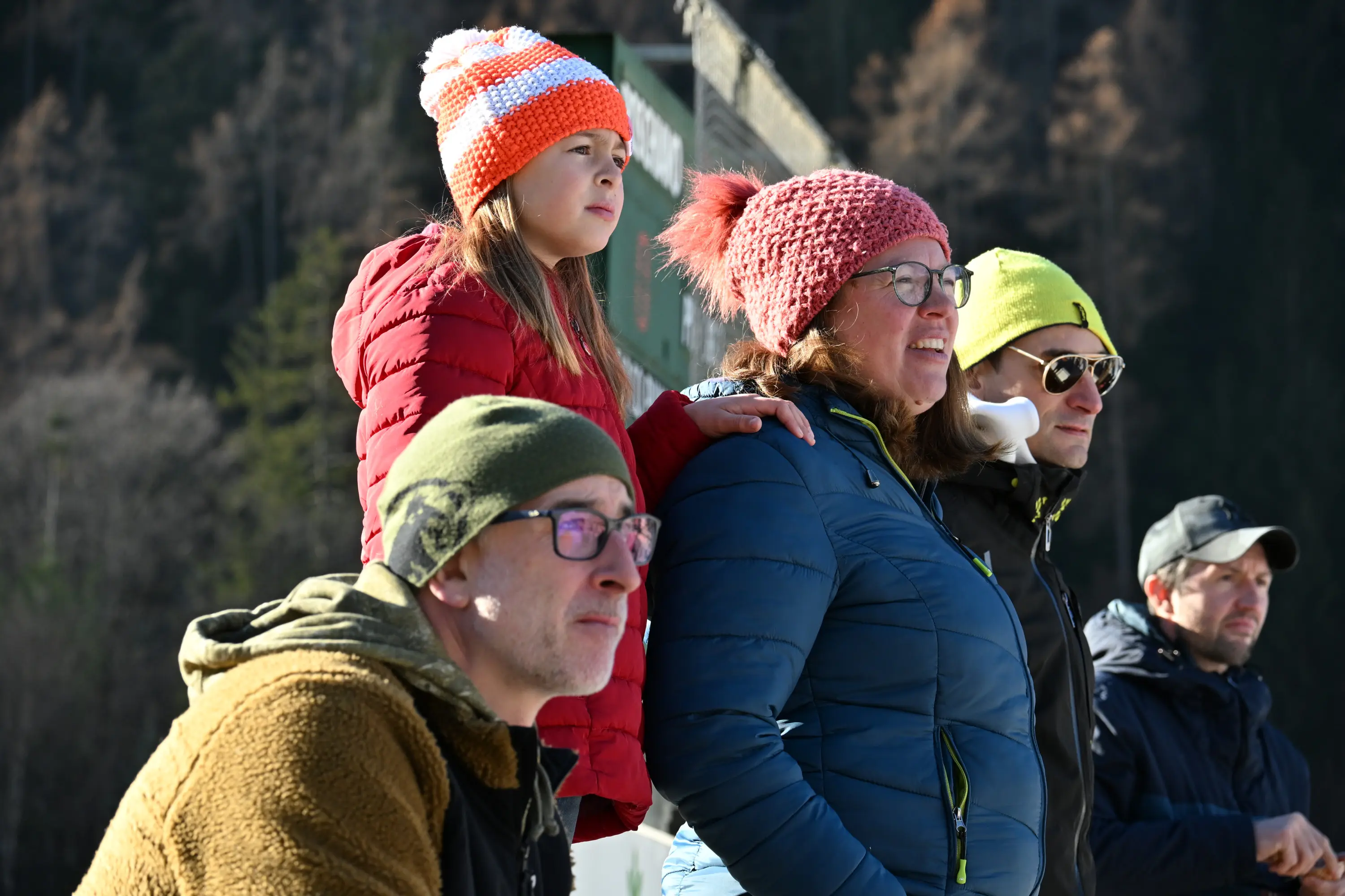 Un gruppo di cinque persone osserva attentamente, con espressioni di interesse. Due adulti indossano berretti e giacche, mentre una giovane ragazza con un cappello a