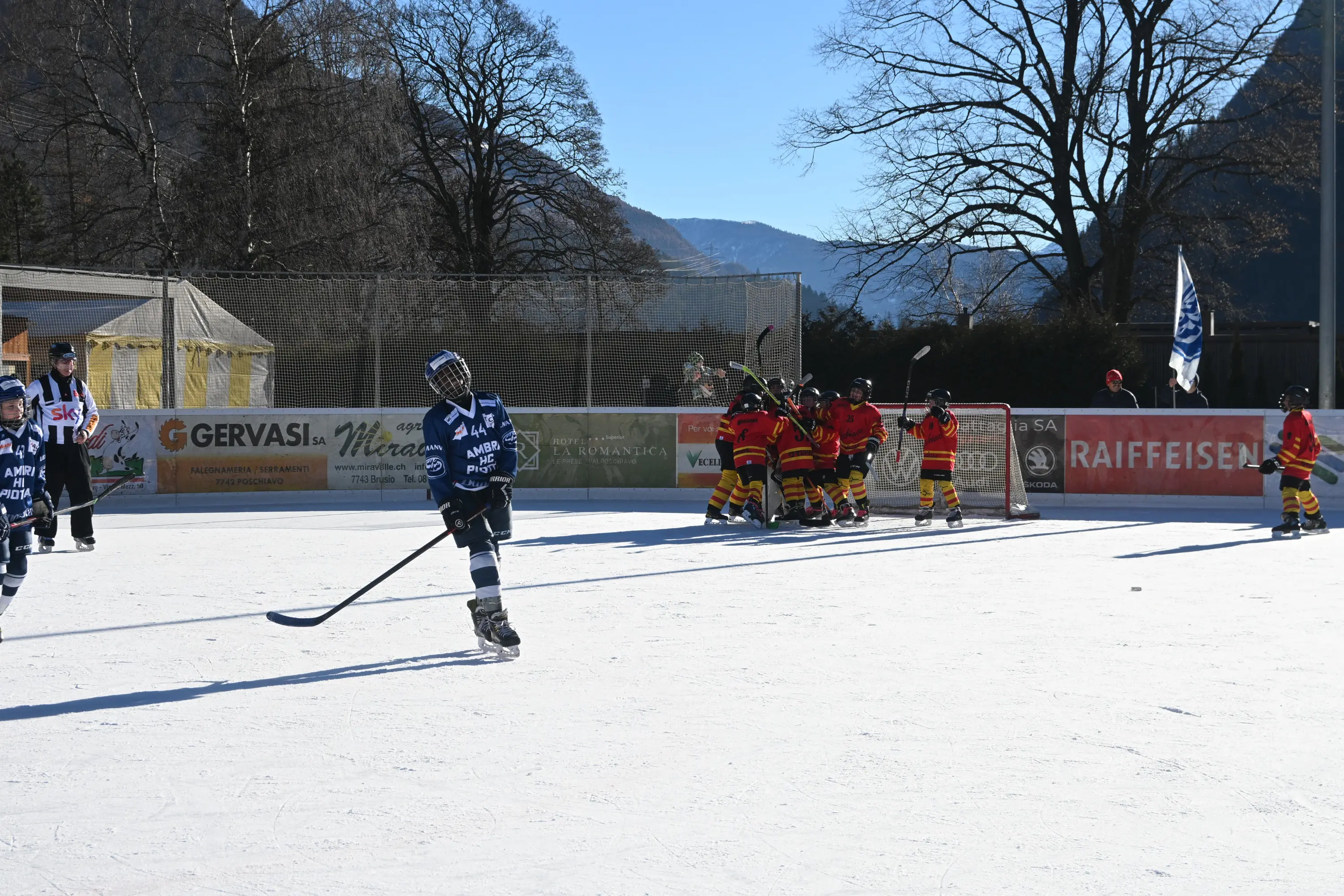 Giocatori di hockey su ghiaccio che si allenano su un campo all'aperto. Un gruppo di giovani in maglietta rossa celebra un gol, mentre un altro giocatore in mag