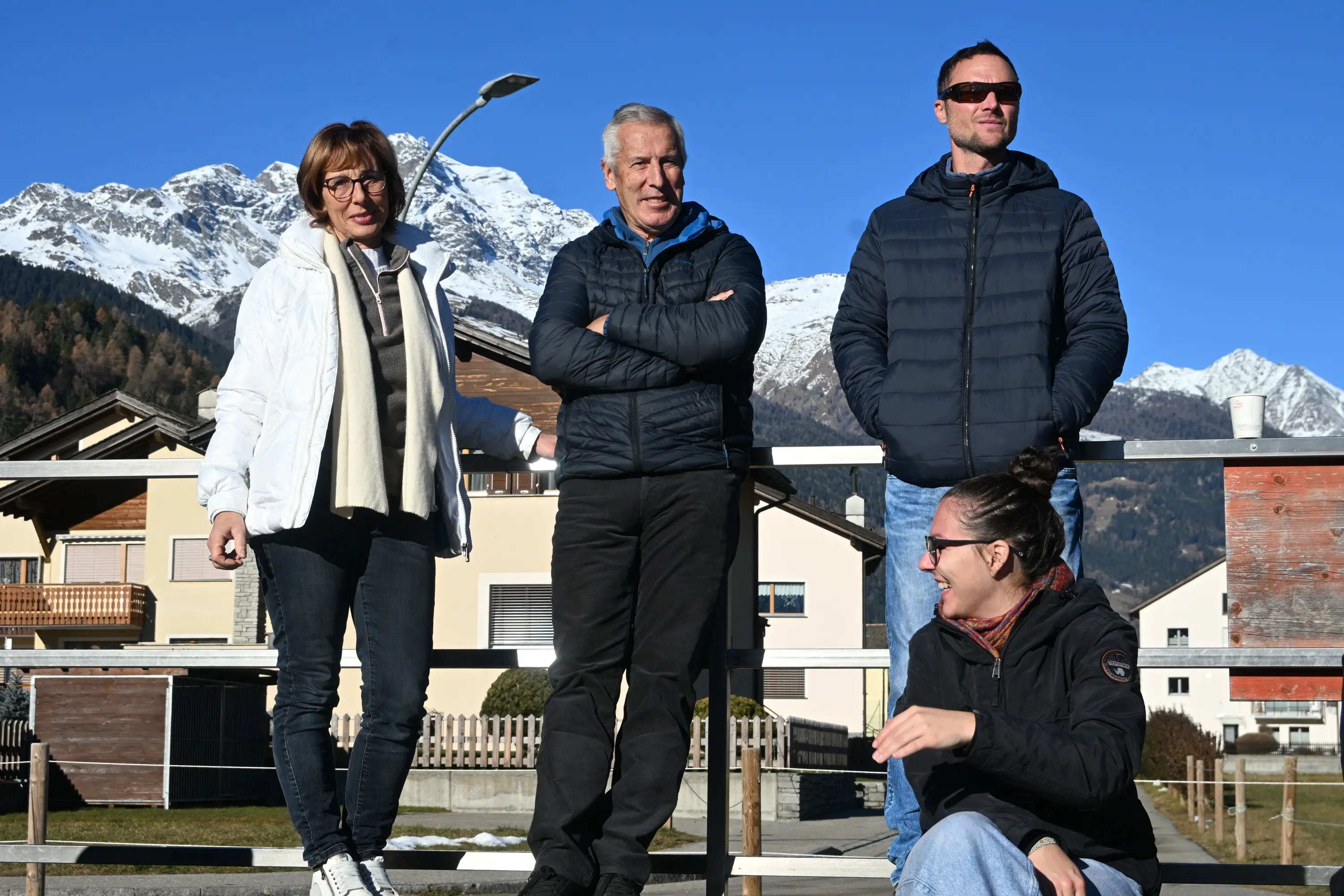 Un gruppo di quattro persone sorride insieme all'aperto, davanti a un paesaggio montano innevato. Due uomini e due donne indossano giacche invernali e sono