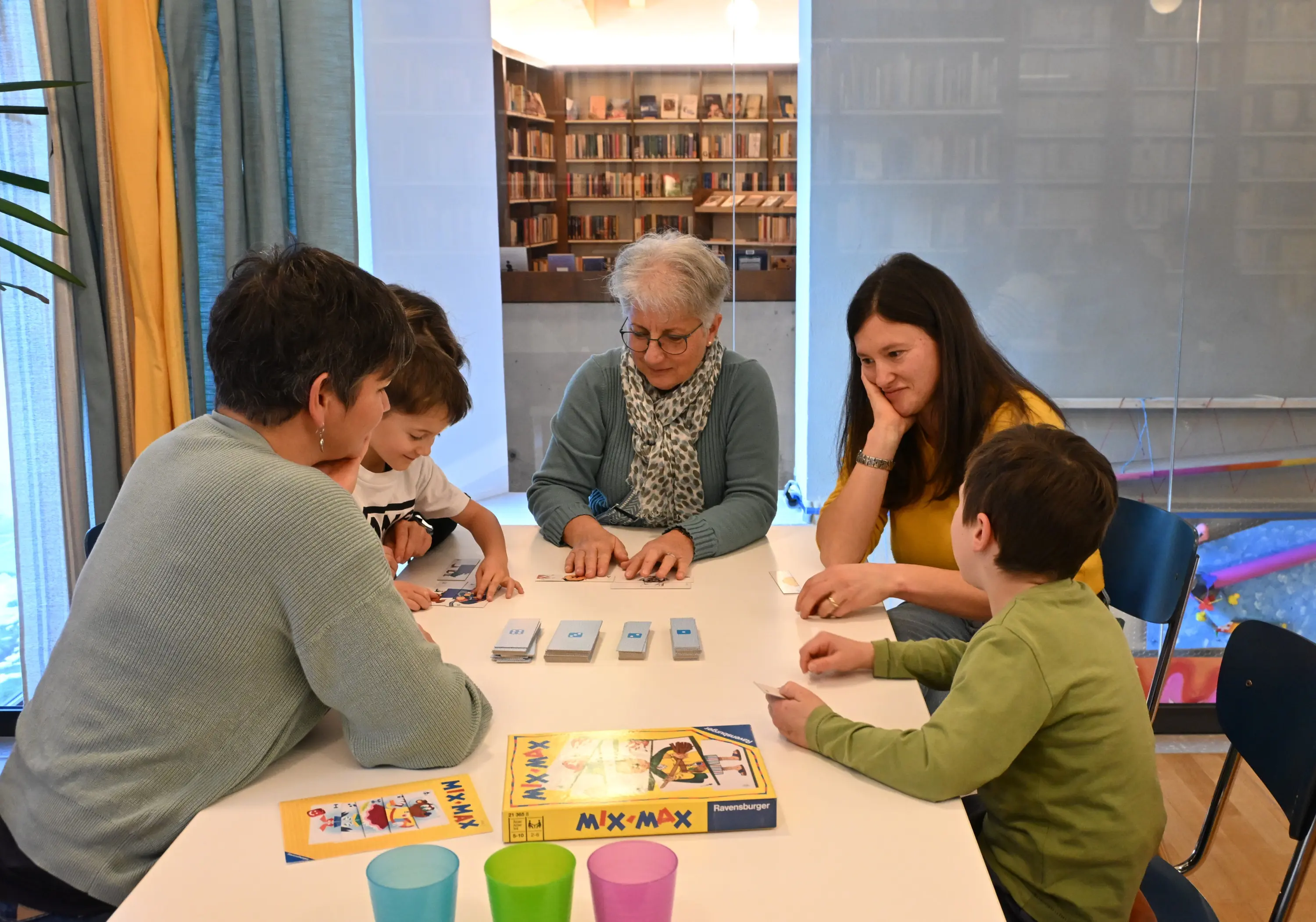 Un gruppo di quattro persone, due adulti e due bambini, si riunisce attorno a un tavolo. Stanno giocando a un gioco da tavolo, con carte e un tab
