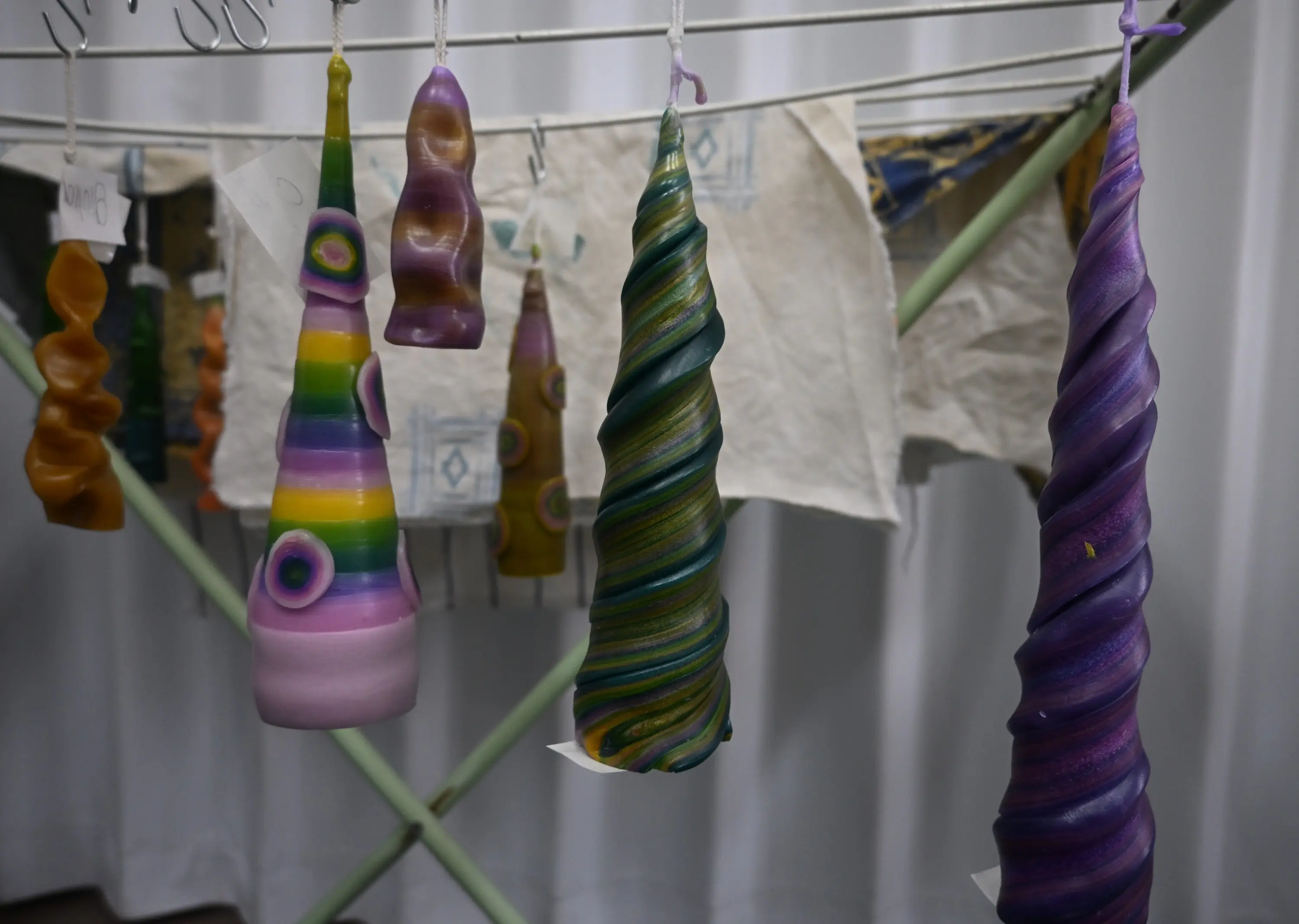 Candele colorate di diverse forme appese a un supporto. Alcune sono spiralate, mentre altre hanno motivi circolari e a strisce.