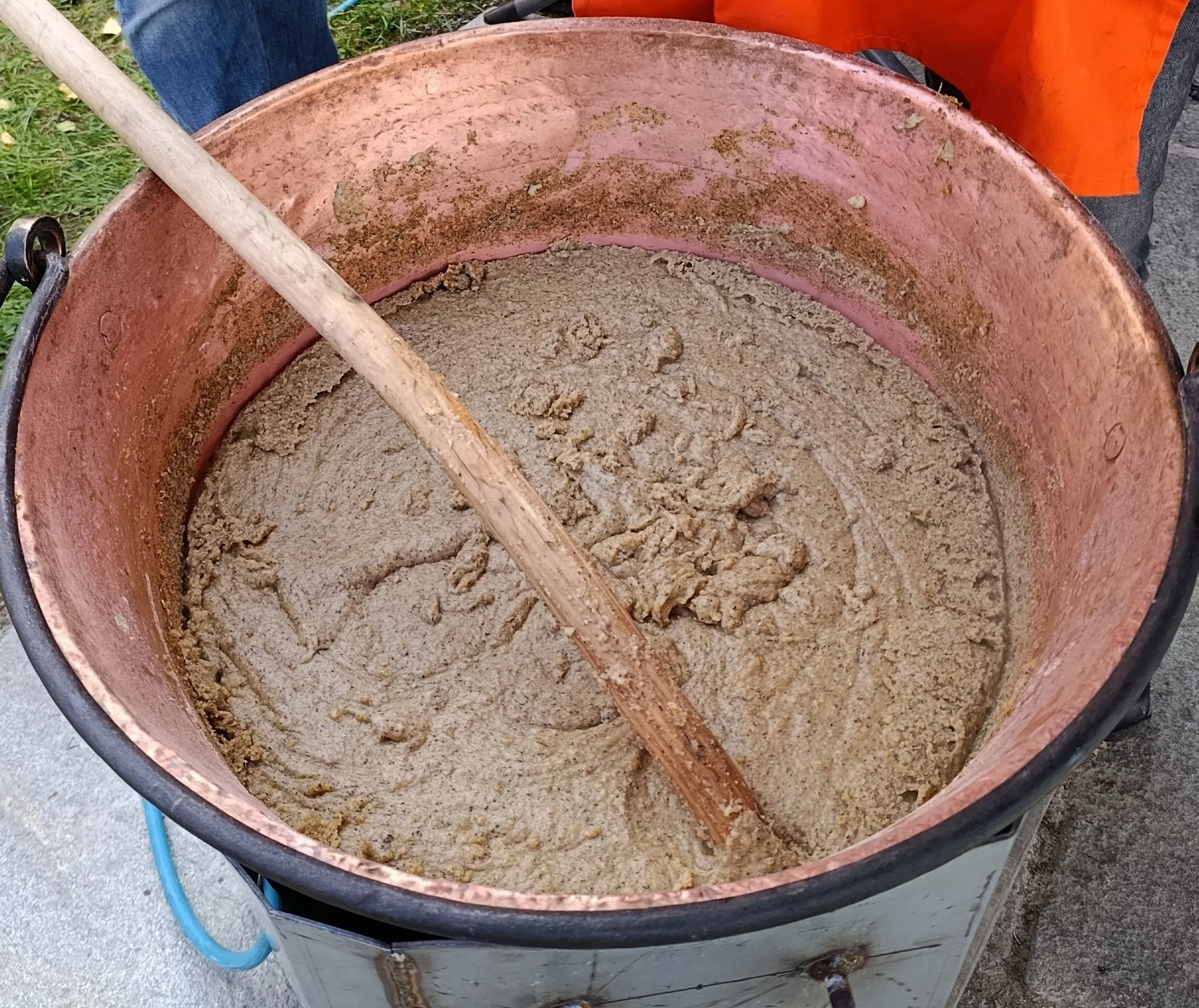 Una grande pentola di rame con un impasto denso e marrone, mescolato con un lungo cucchiaio di legno.