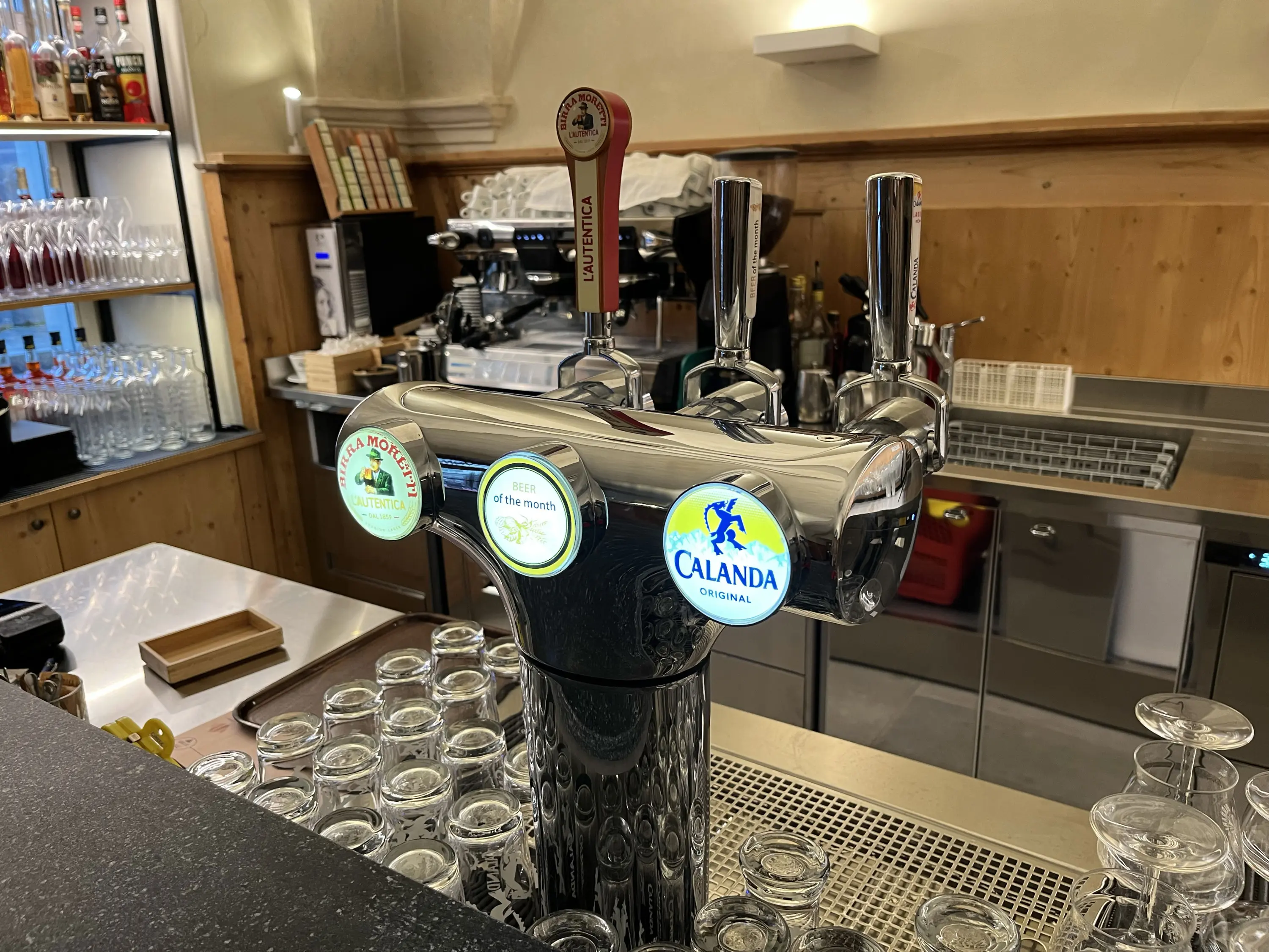 Un bancone bar con un erogatore di birra in acciaio lucido. Ci sono tre rubinetti, due dei quali mostrano i loghi di birre diverse. Sul