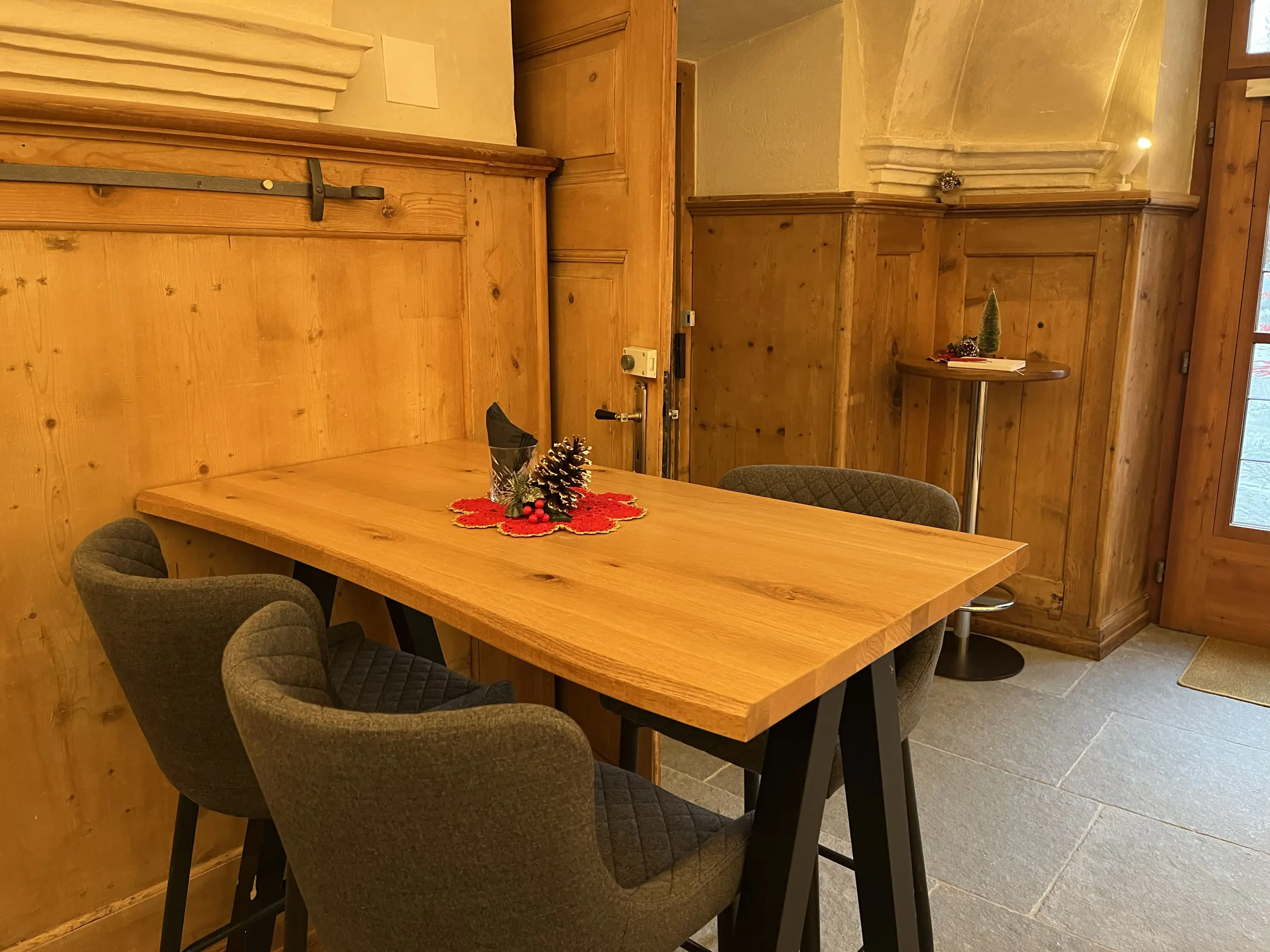 Un tavolo in legno con sedie grigie, decorato con un centrotavola natalizio, in un ambiente con pareti di legno e un'atmosfera accogl