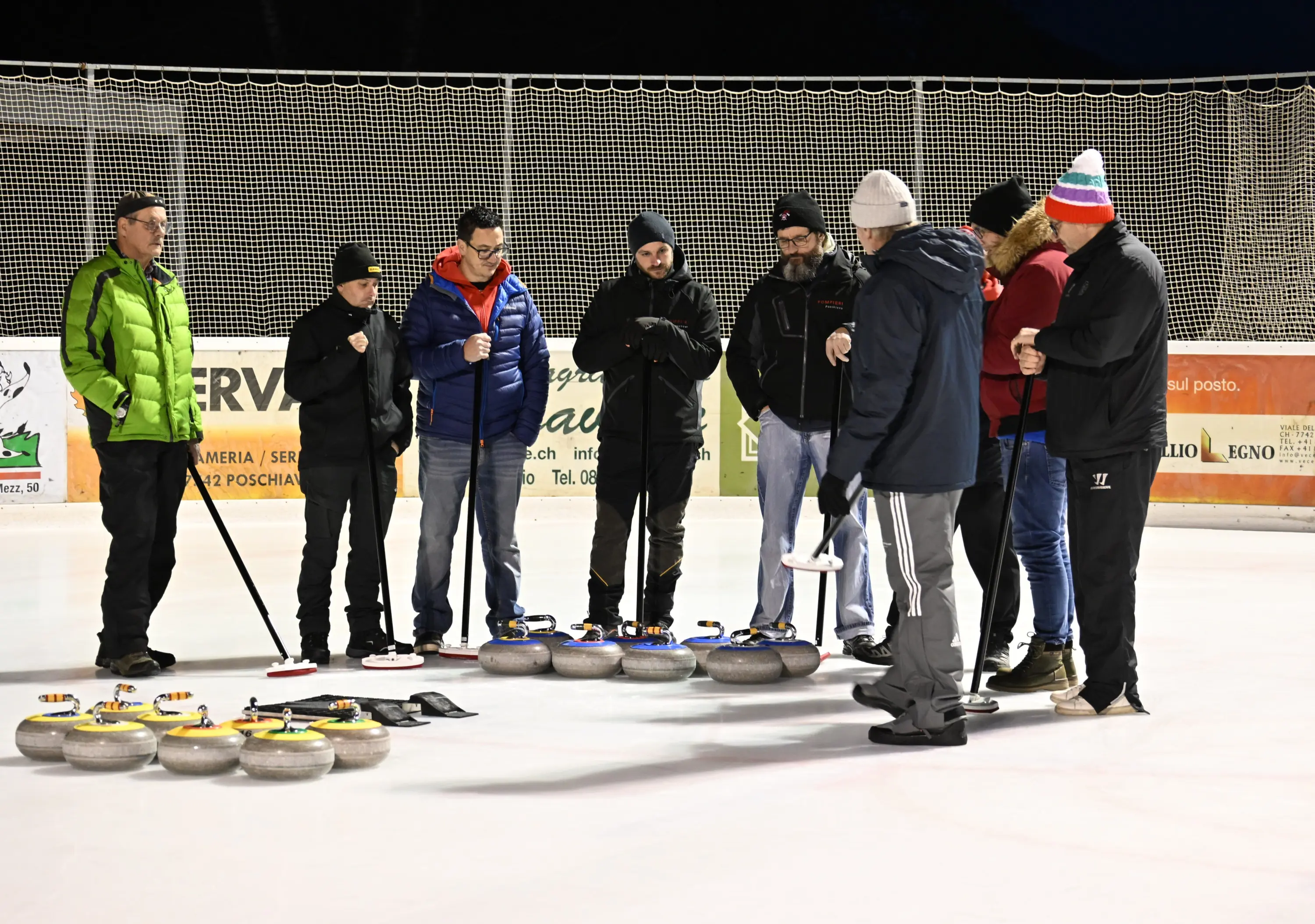 Un gruppo di persone si riunisce sul ghiaccio per una sessione di curling. Alcuni indossano abbigliamento invernale, come giacche pesanti e berrette