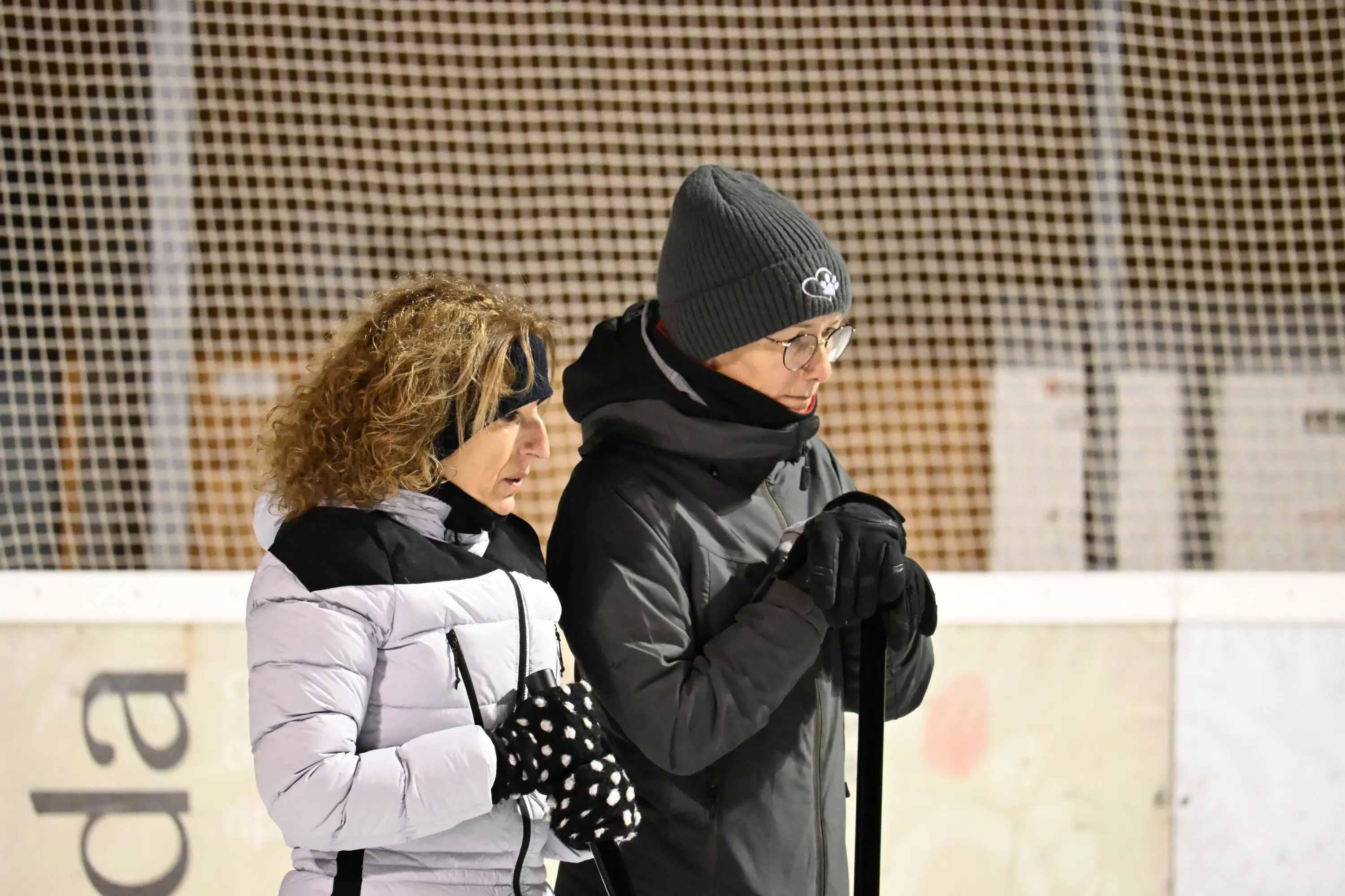 Due persone vestite in abbigliamento invernale, una con capelli ricci e guanti a pois, l'altra in un cappello grigio e occhiali, osservano