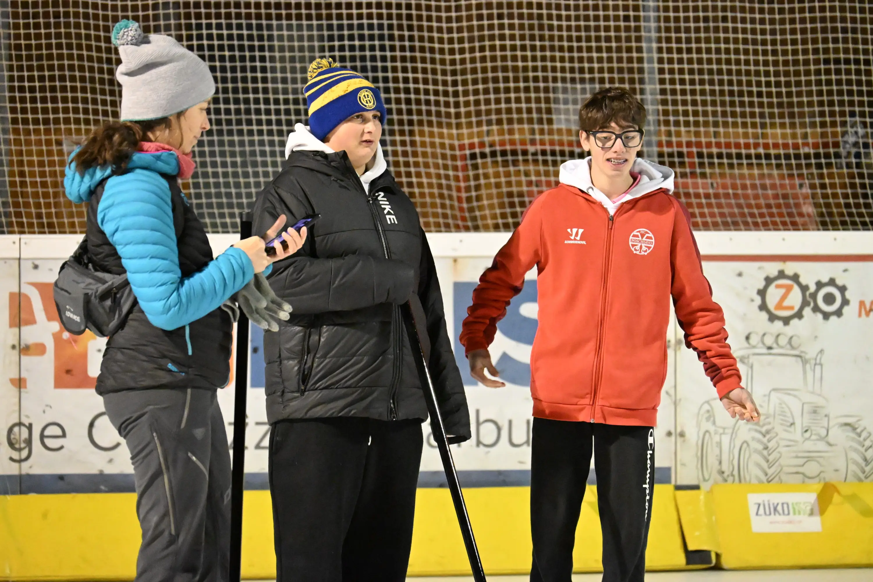 Tre persone su una pista di pattinaggio. Due donne stanno parlando, una indossa un berretto blu e l'altra una giacca nera. Un ragazzo in un giubbot