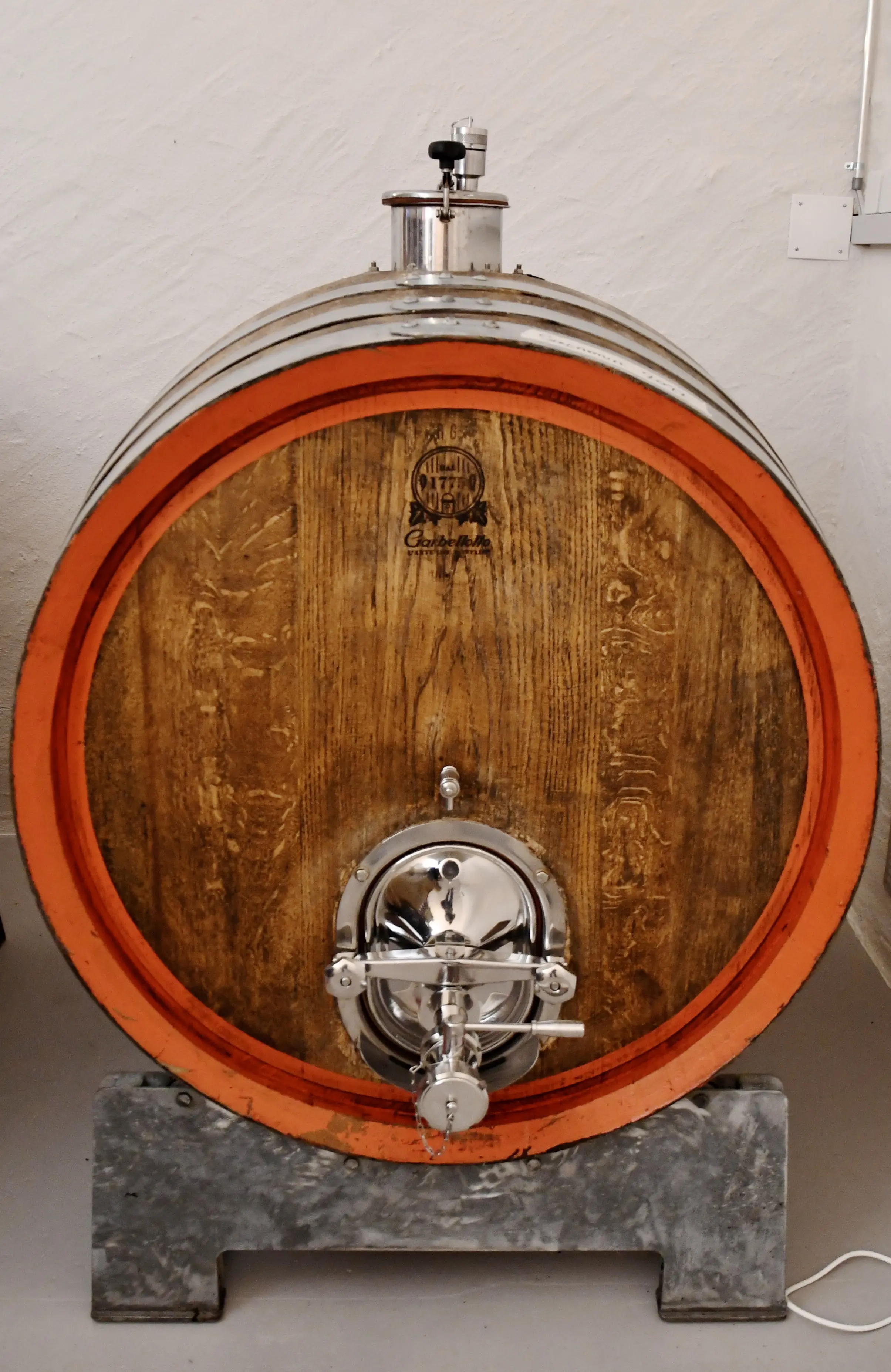 Botte di legno con un tappo metallico, poggiata su una base di metallo, in un ambiente interno.