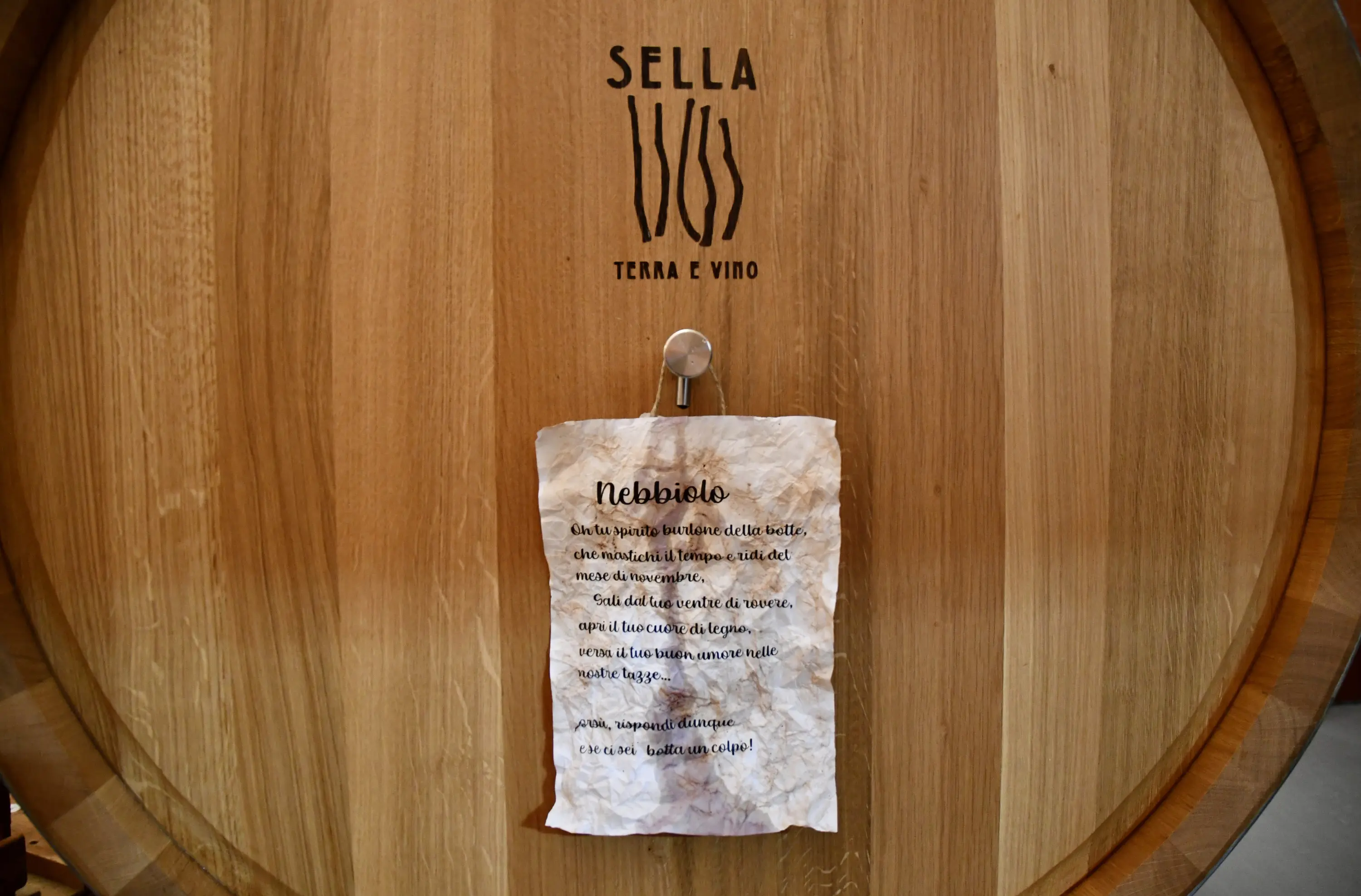Barile di legno con il nome "Sella - Terra e Vino" inciso. Appesa, una nota ingiallita descrive il Nebbiolo, un vino tipico.