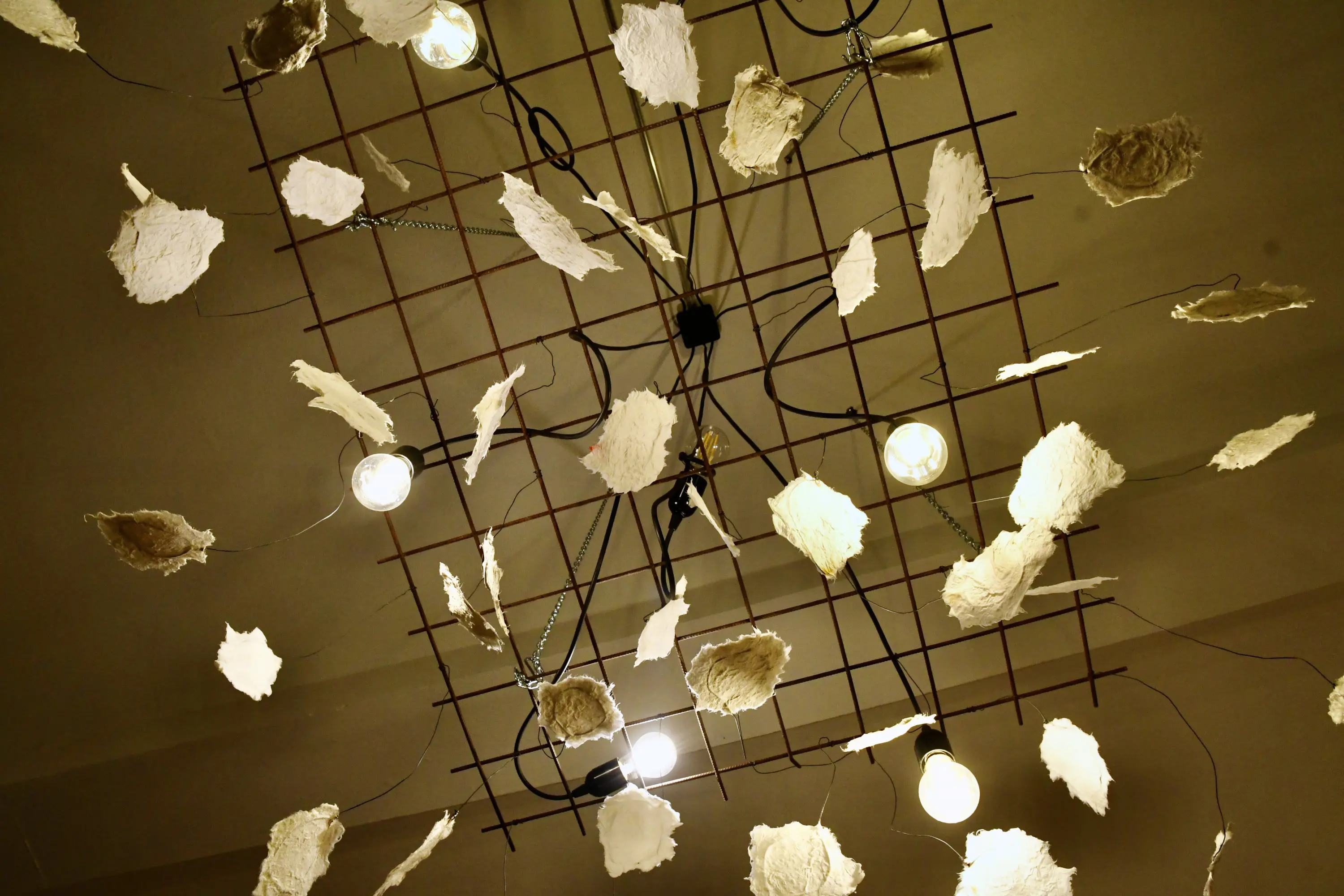 Lampadario moderno con una struttura metallica e elementi decorativi in carta, illuminato da lampadine che emettono una luce calda.