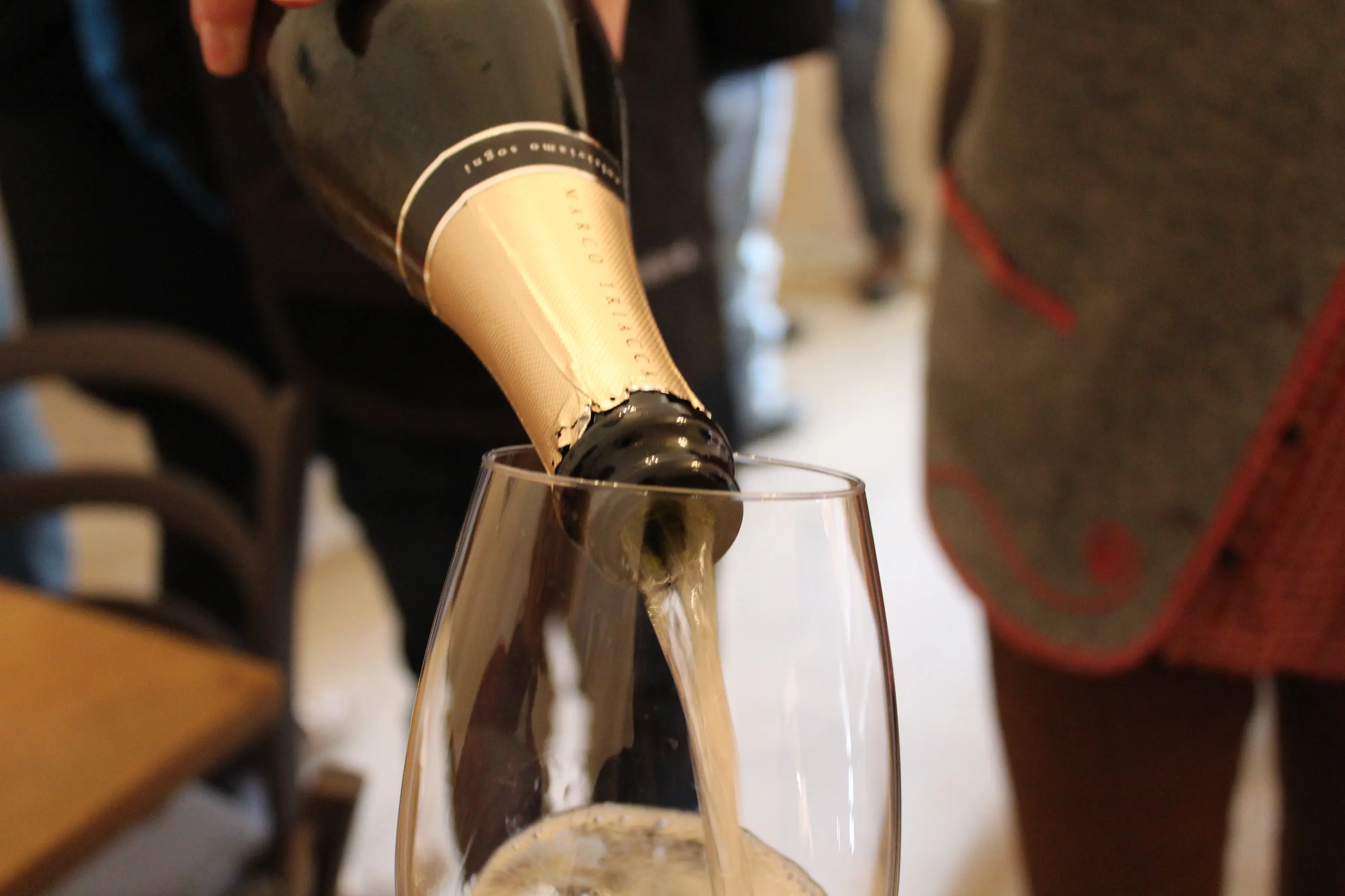 Un flautino viene riempito con champagne mentre una persona versa dalla bottiglia. Si vede la schiuma frizzante emergere nel bicchiere.